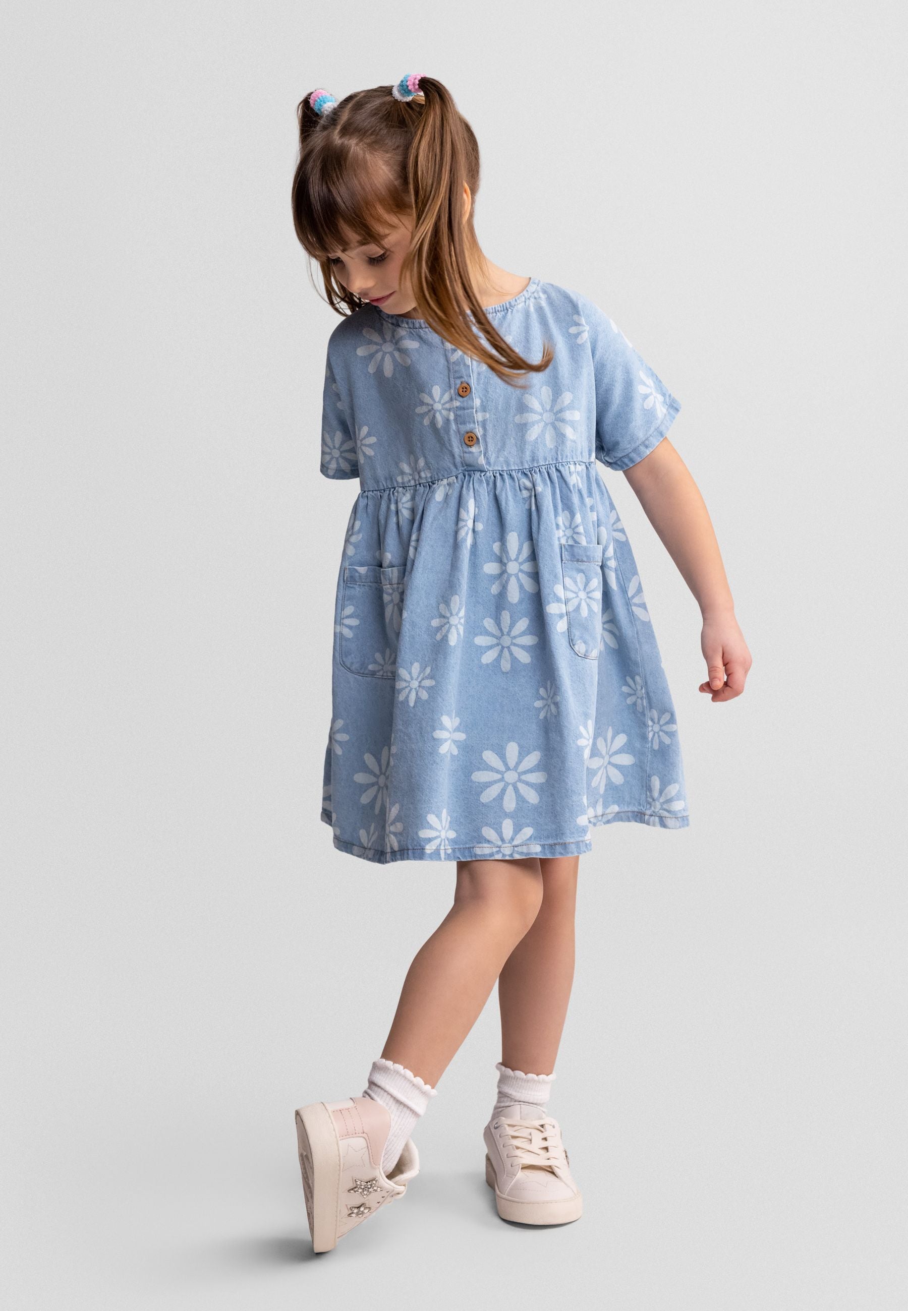 Flat lay of blue chambray dress with white daisy print pattern, showing short sleeves and gathered skirt design on white background