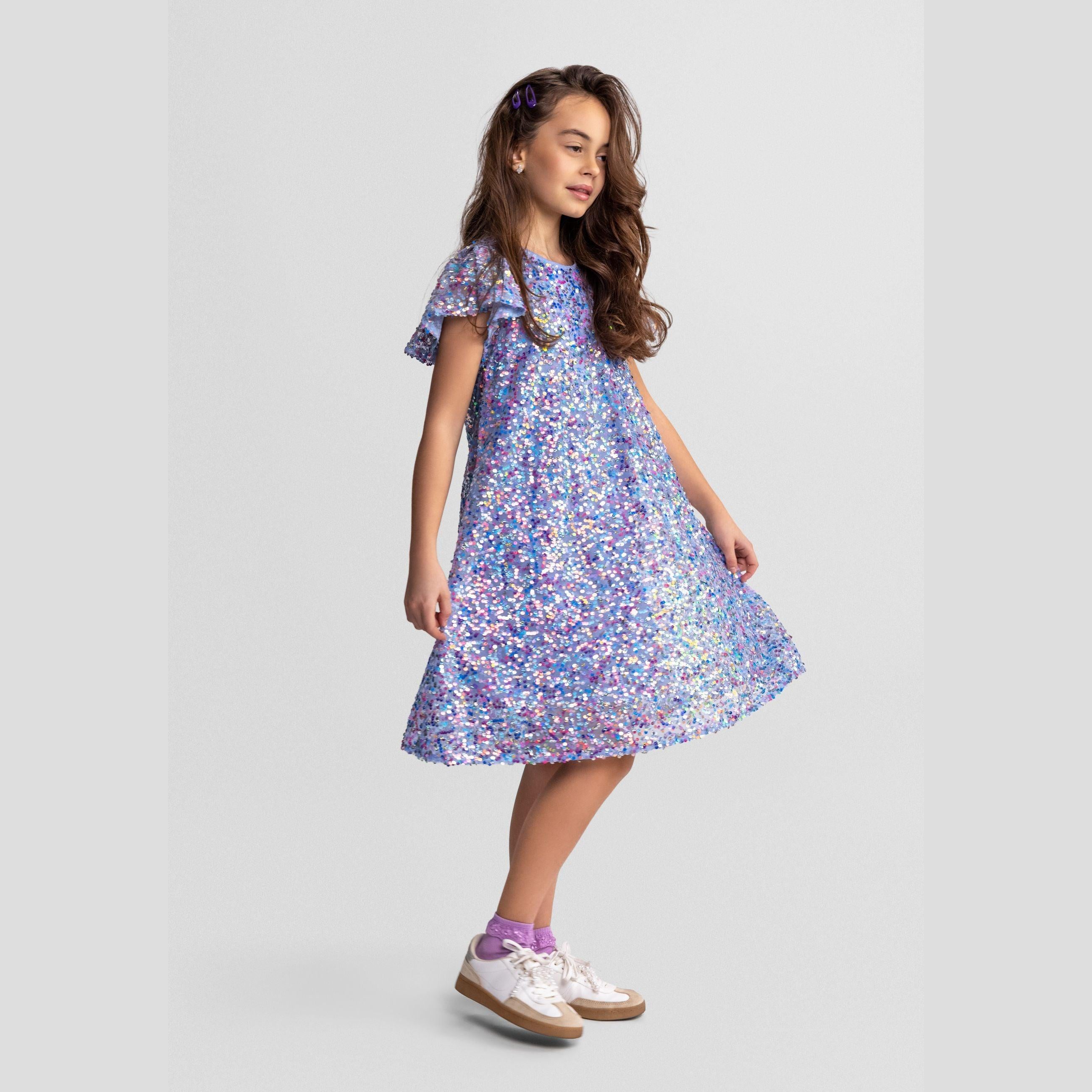 Girl wearing blue sequin party dress with A-line silhouette and flared sleeves, standing against light grey background