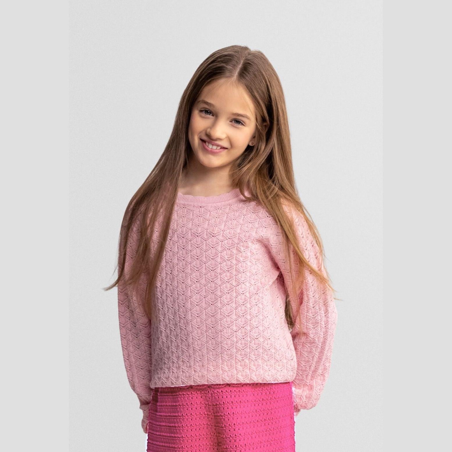 Young girl wearing pink wave hem jumper with bright pink skirt, smiling against white studio background