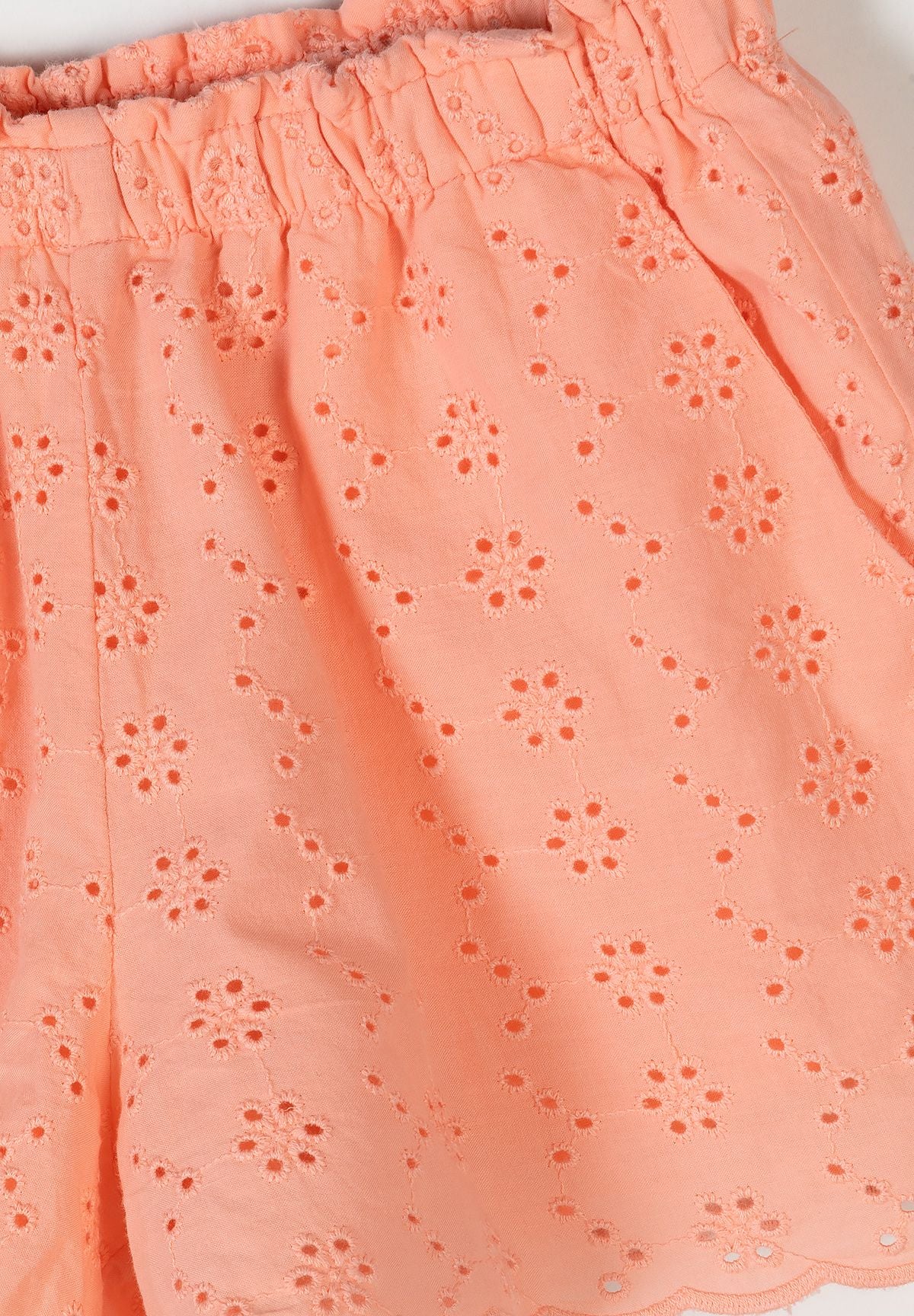 Close-up detail of apricot cotton fabric showing delicate broderie anglaise eyelet embroidery pattern with floral motifs and elasticated waistband