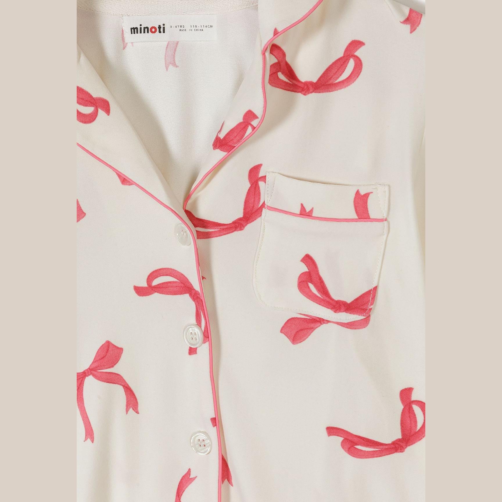 Detail shot of pyjama top showing Minoti brand label, button closure, chest pocket and pink bow print on cream fabric