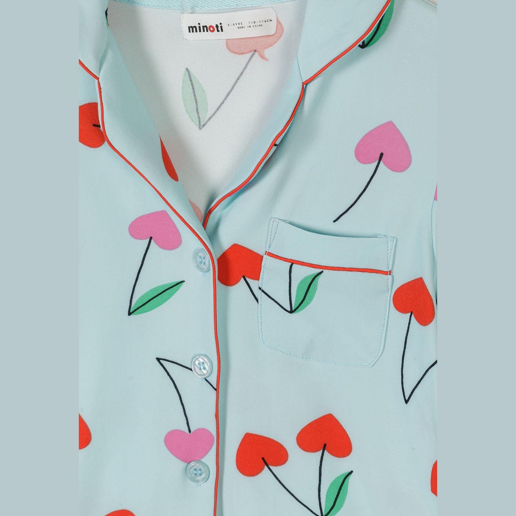 Detail shot of light blue pajama top showing Minoti label, red piping trim, cherry print pattern and button closure