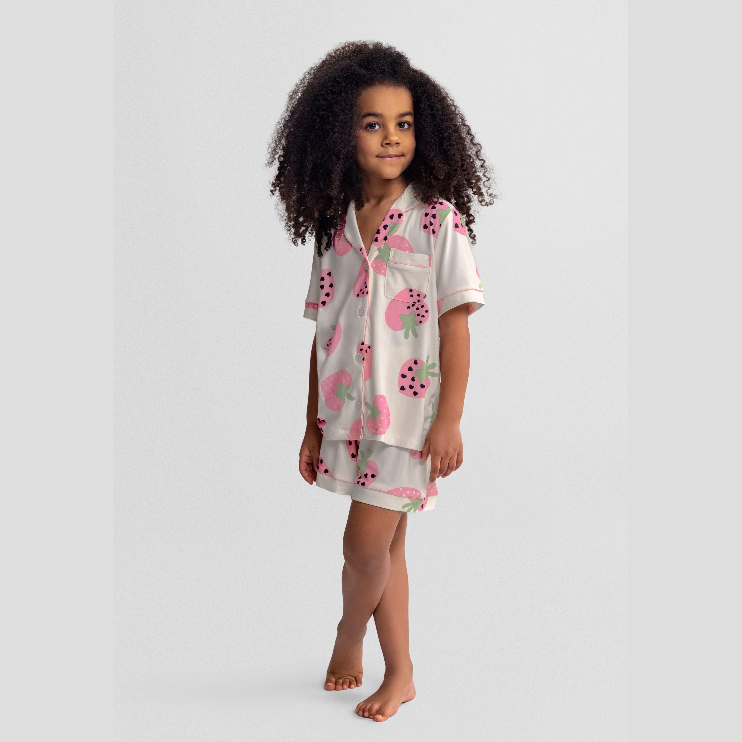 Pink pyjama set laid flat showing short sleeve button-up top with collar and pocket, matching elasticated shorts with white piping trim