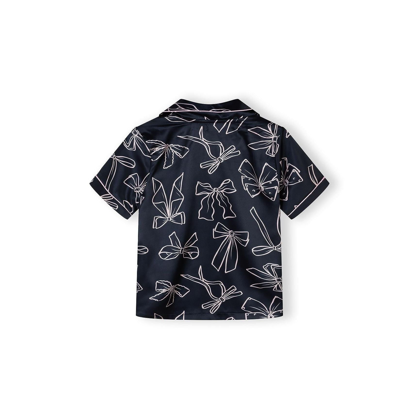 Detail view of navy satin pyjama top showing lapel collar, button placket, chest pocket and bow print pattern with Minoti label visible