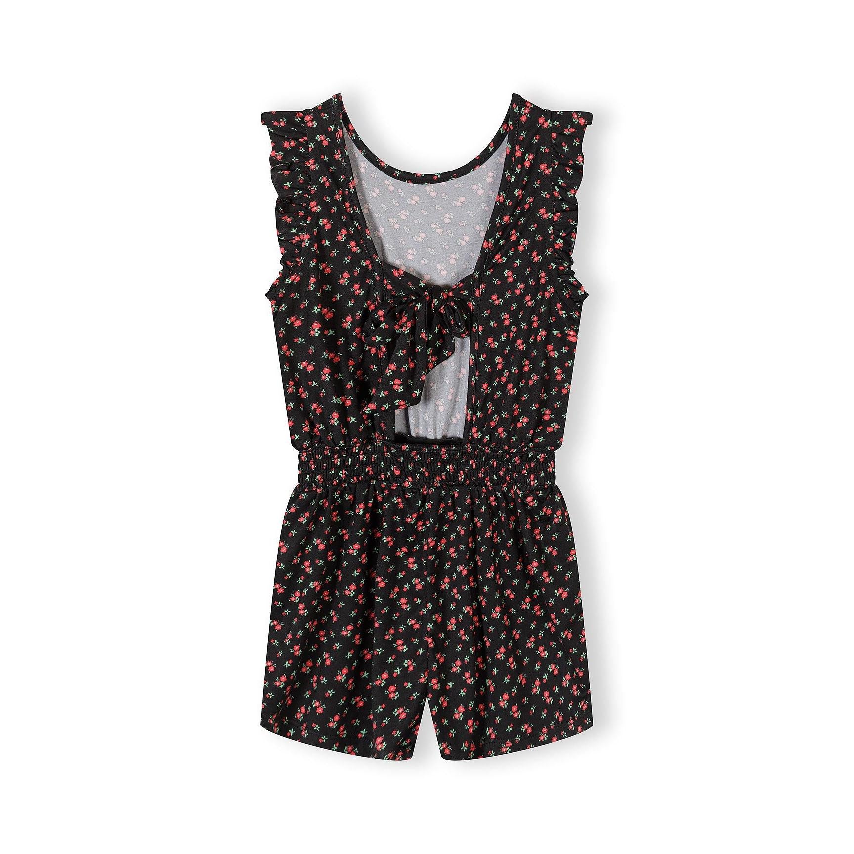 Back view of black floral jumpsuit showing tie-back detail and white vest underneath, flat lay on white background