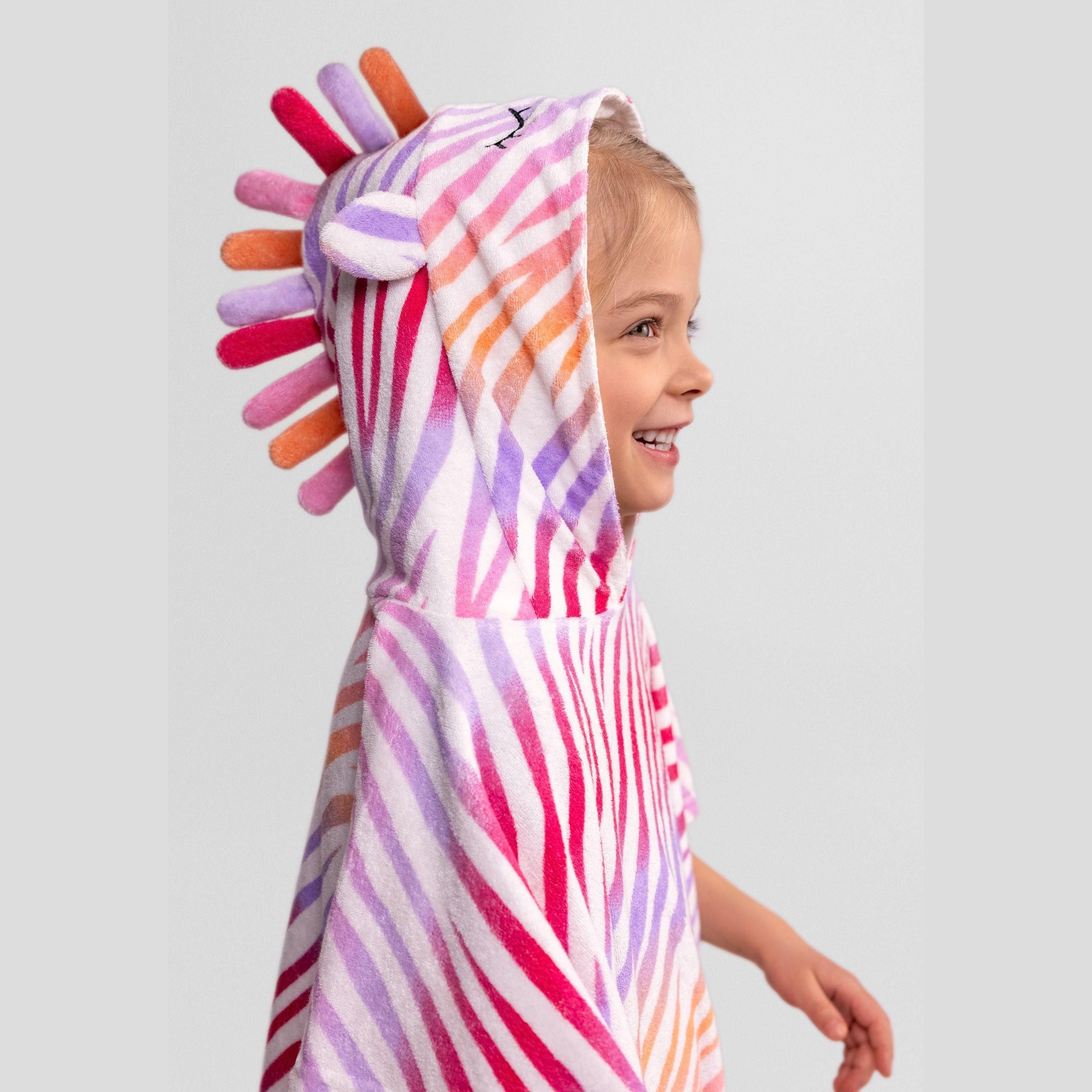 Young girl wearing multicoloured zebra print towelling hooded cover-up with rainbow fabric spikes on hood, shown from side profile against white background