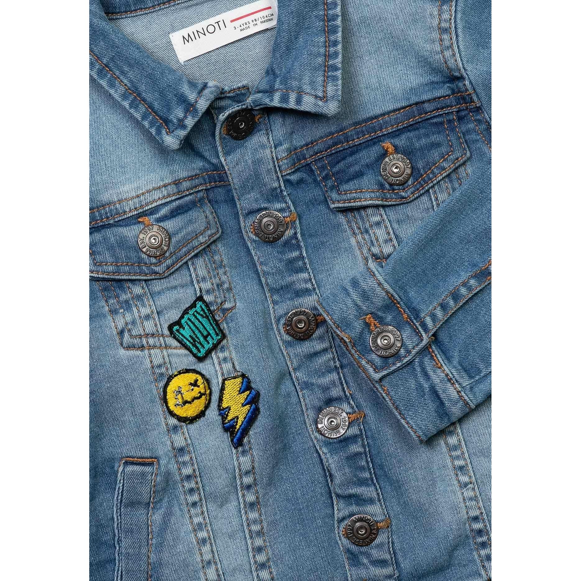 Close-up detail of Minoti label and embroidered badges including smiley face and lightning bolt on light blue denim