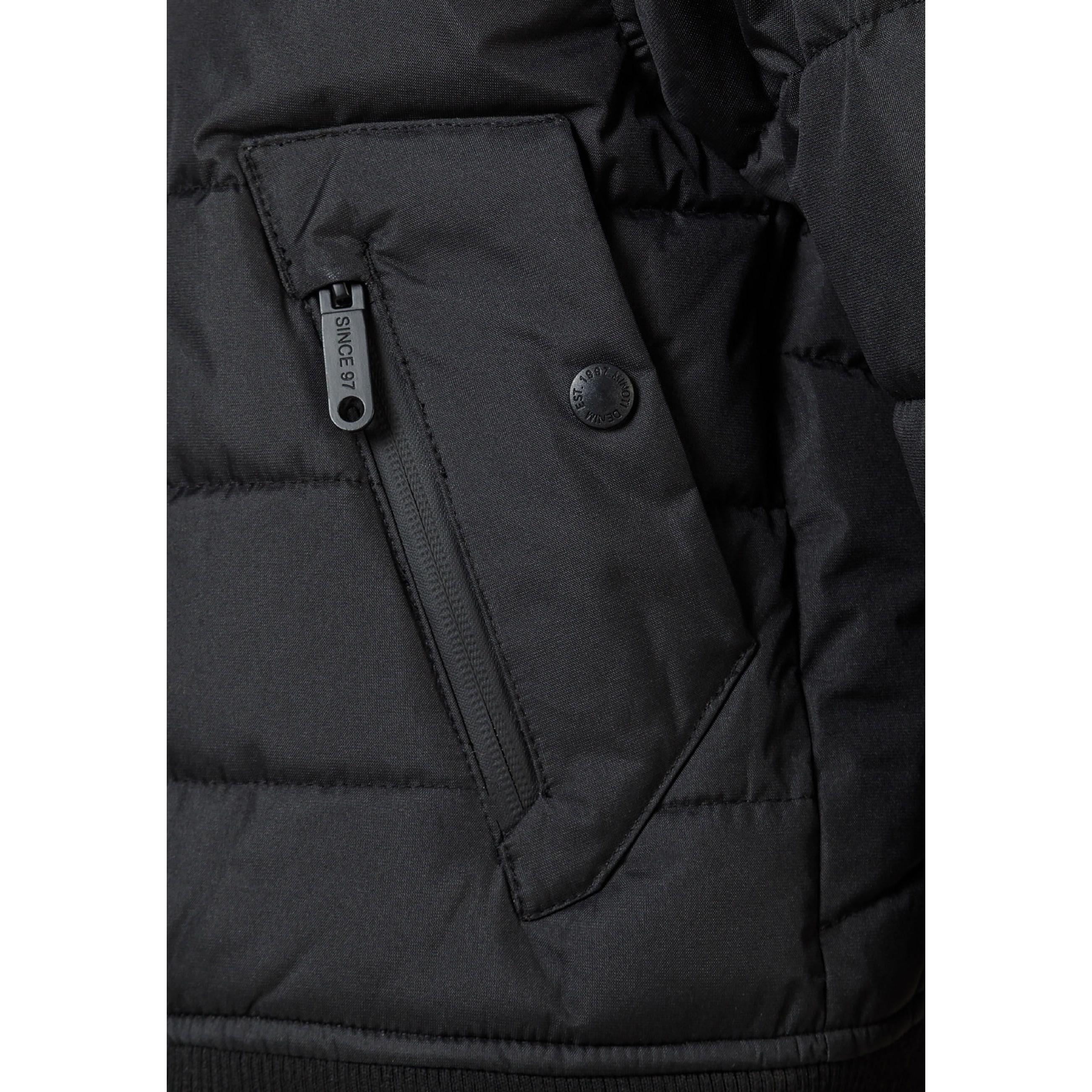 Close-up detail of black circular Minoti logo patch on the sleeve of the padded jacket showing MT 97 branding