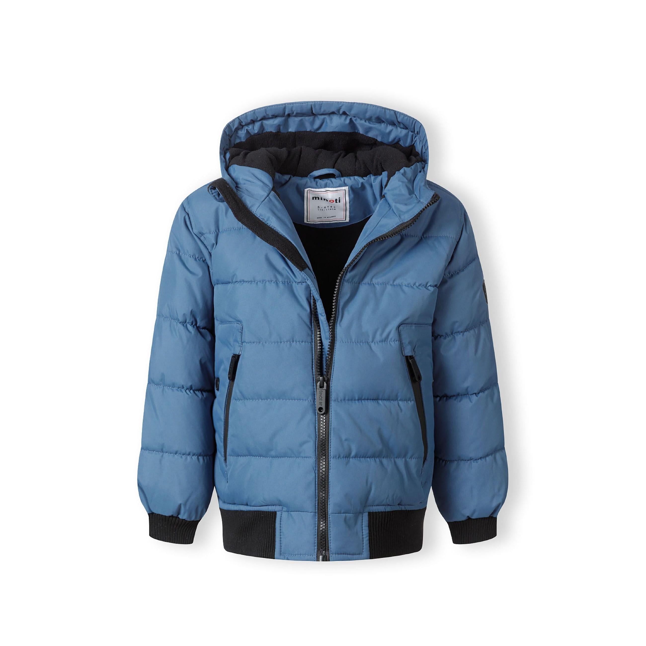 Close-up detail of blue padded jacket showing circular Minoti logo patch with cross design