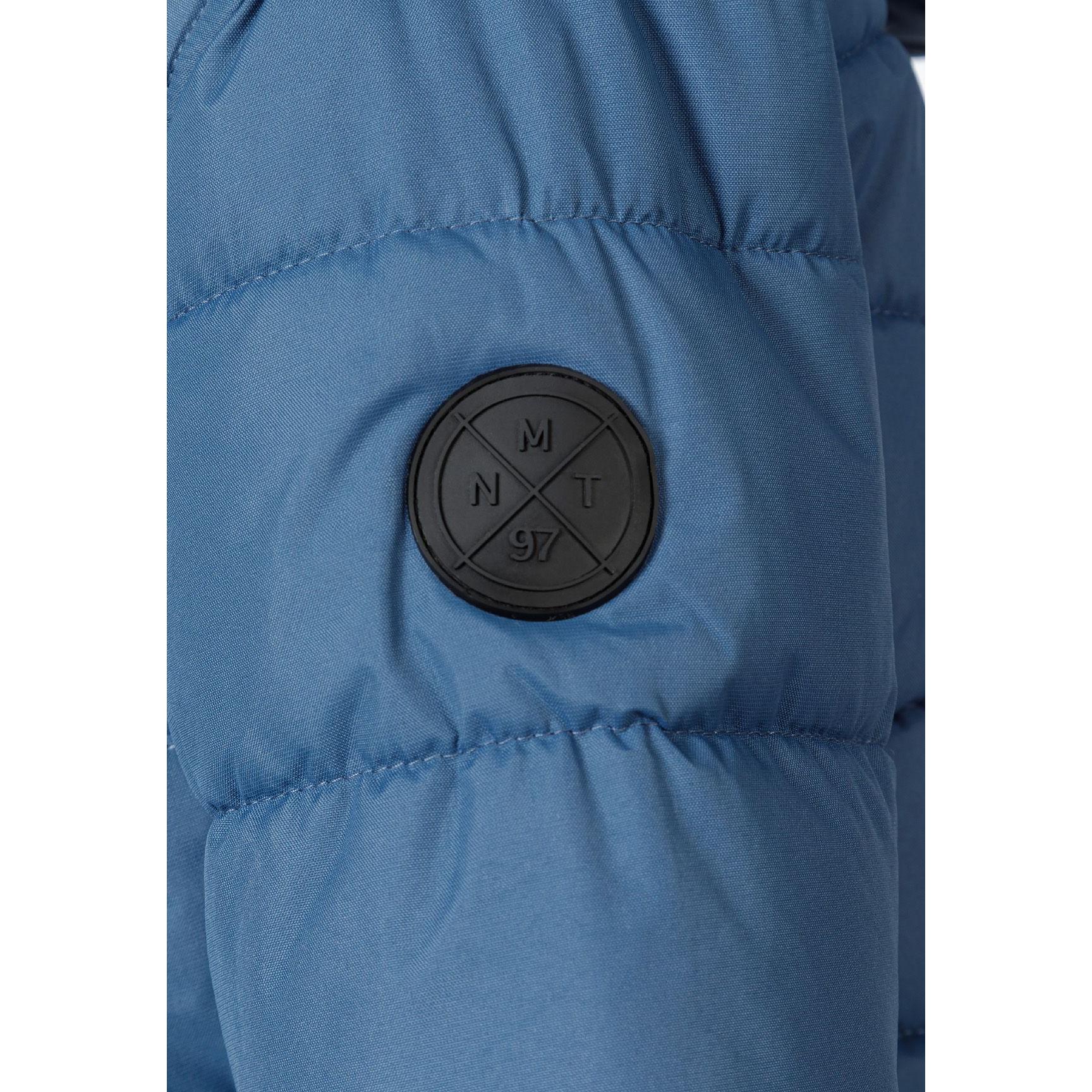 Close-up detail of blue padded jacket showing circular Minoti logo patch with cross design