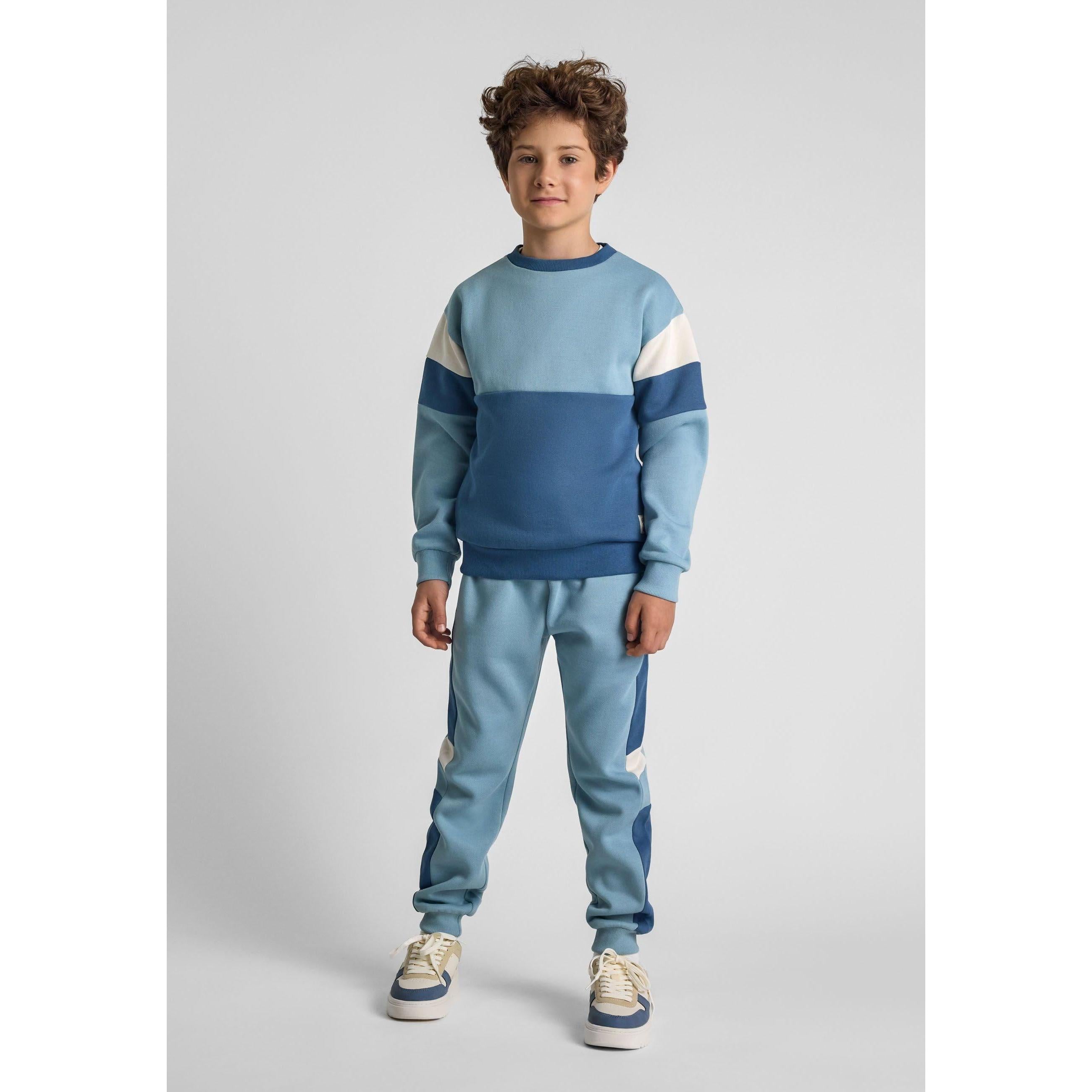Boy wearing blue colourblock tracksuit set with matching sweatshirt and joggers against light grey background