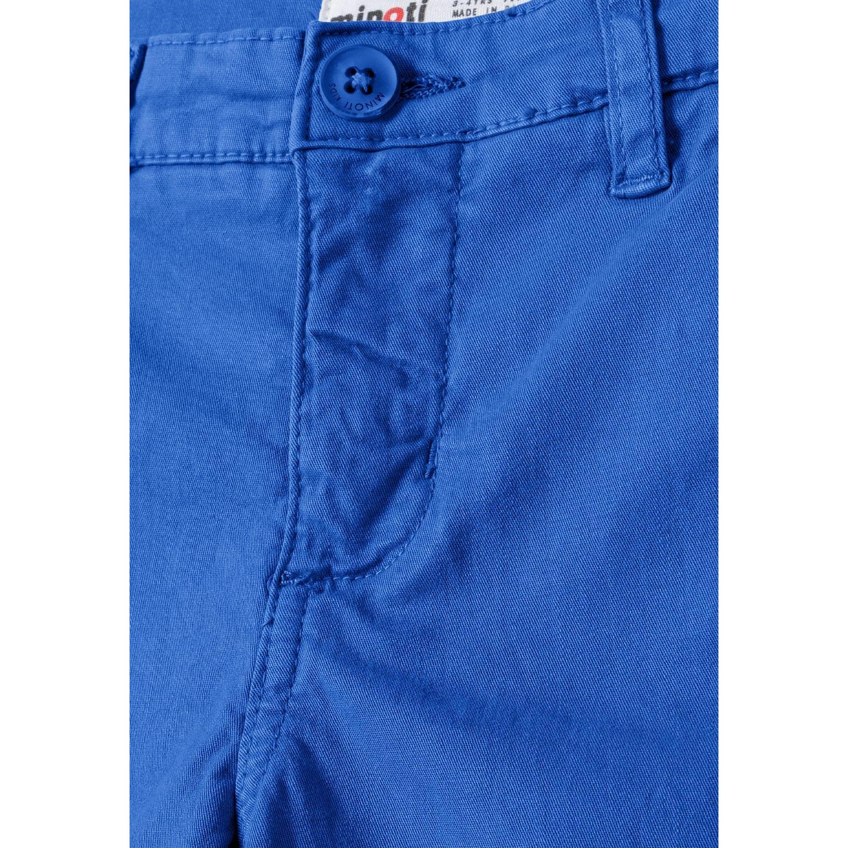 Close-up detail of cobalt blue chino shorts showing Minoti brand label, button fastening and fabric texture