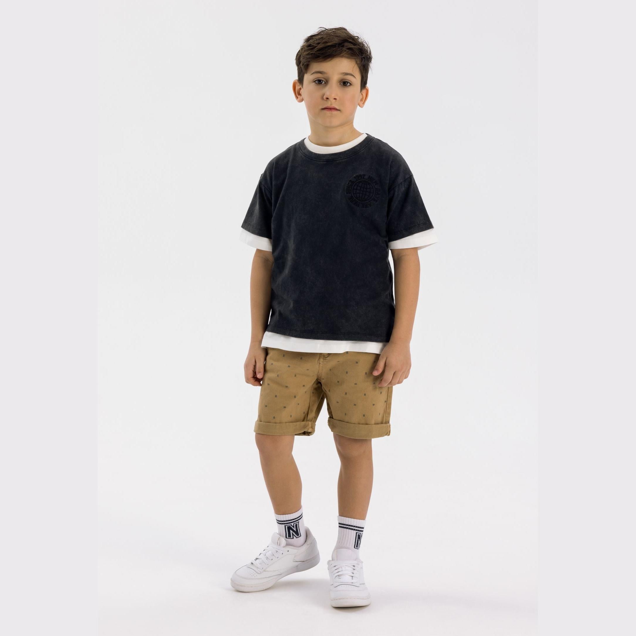 Boy wearing beige chino shorts with small print pattern and navy t-shirt on white background