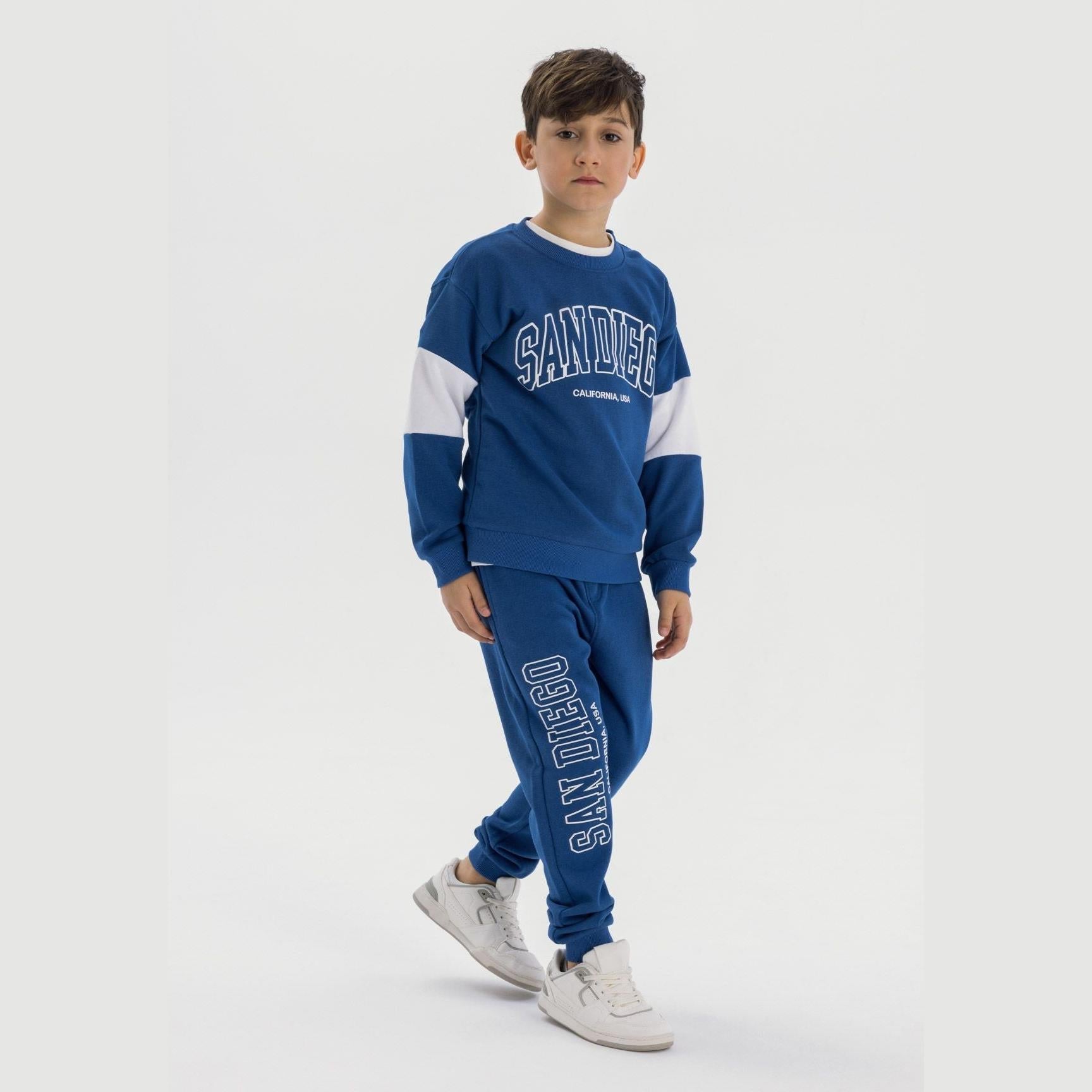 Boy wearing cobalt blue tracksuit set with San Diego print, full body view on light grey background showing sweatshirt with white sleeve panels and matching joggers