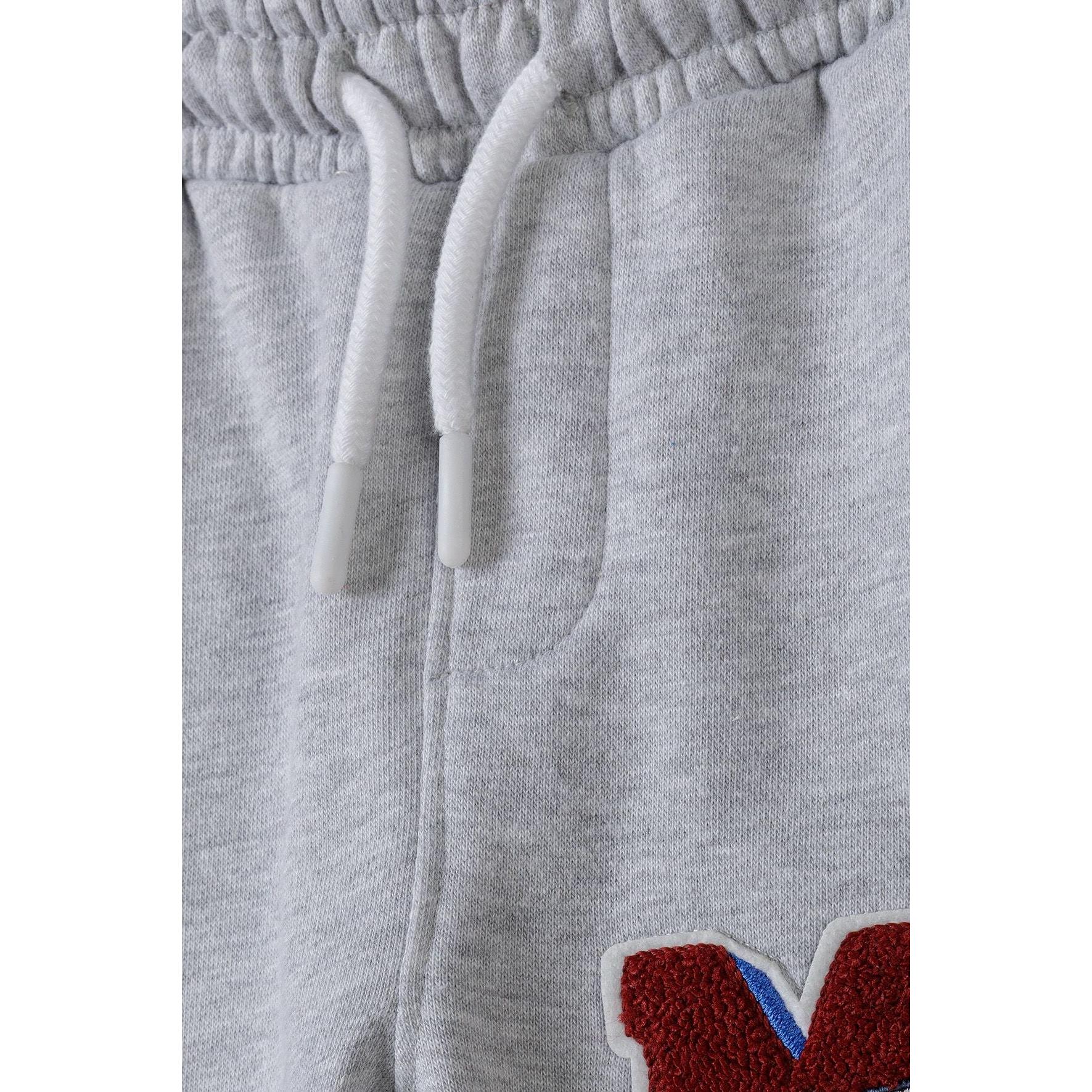 Close-up detail of grey fleece fabric texture, drawstring waistband and red M applique with blue accent