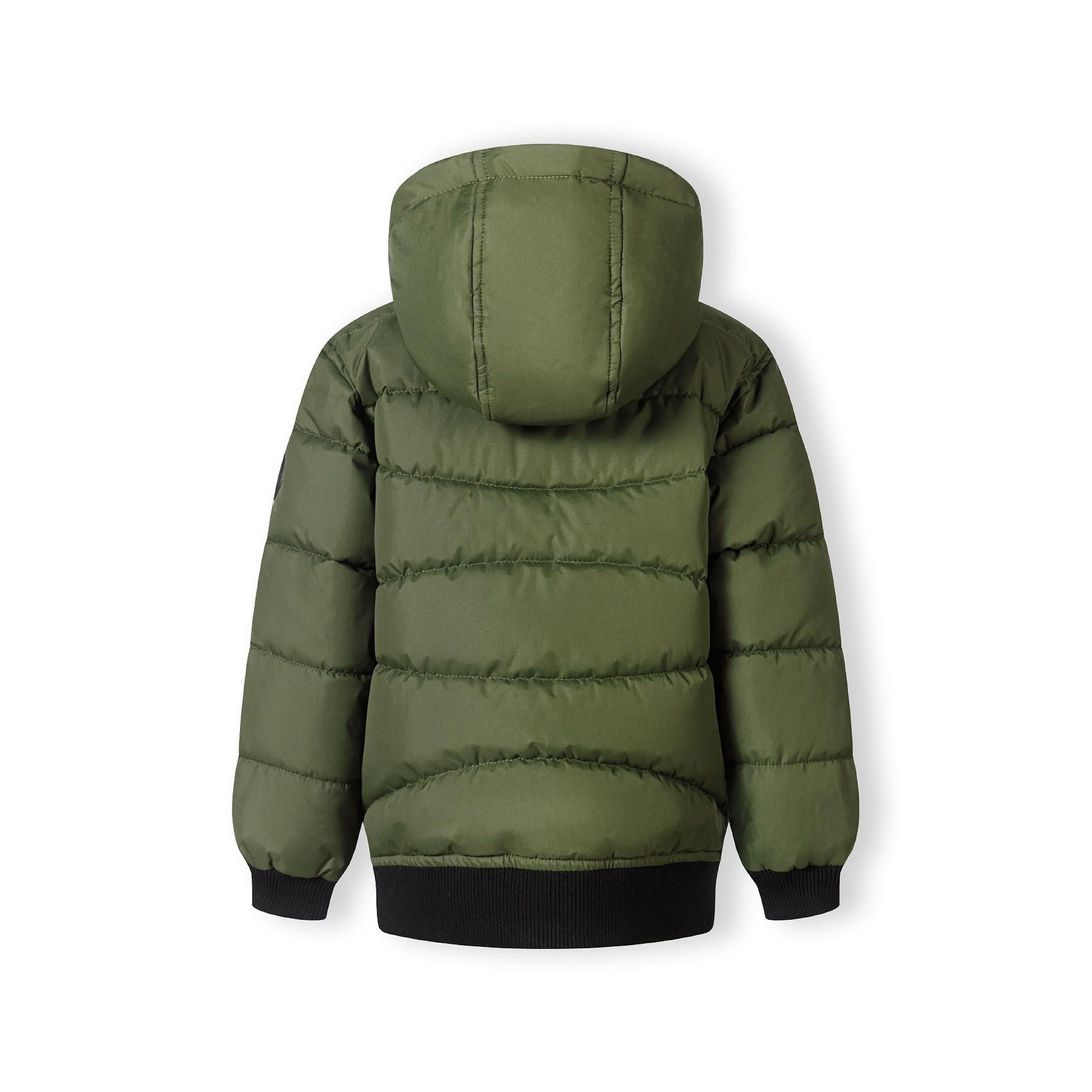 Close-up detail of khaki padded jacket showing circular black Minoti brand badge with crossed design and number 97