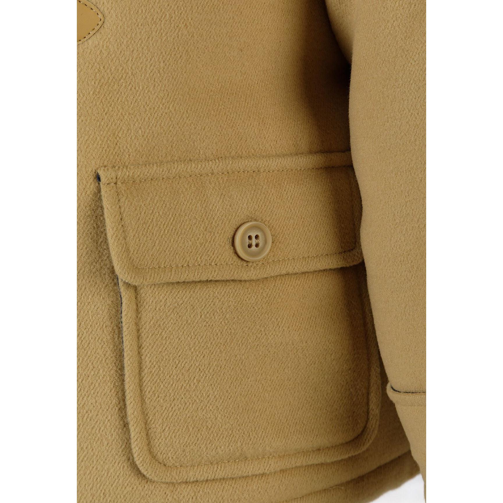 Close-up detail of beige duffle jacket flap pocket with button fastening showing fabric texture