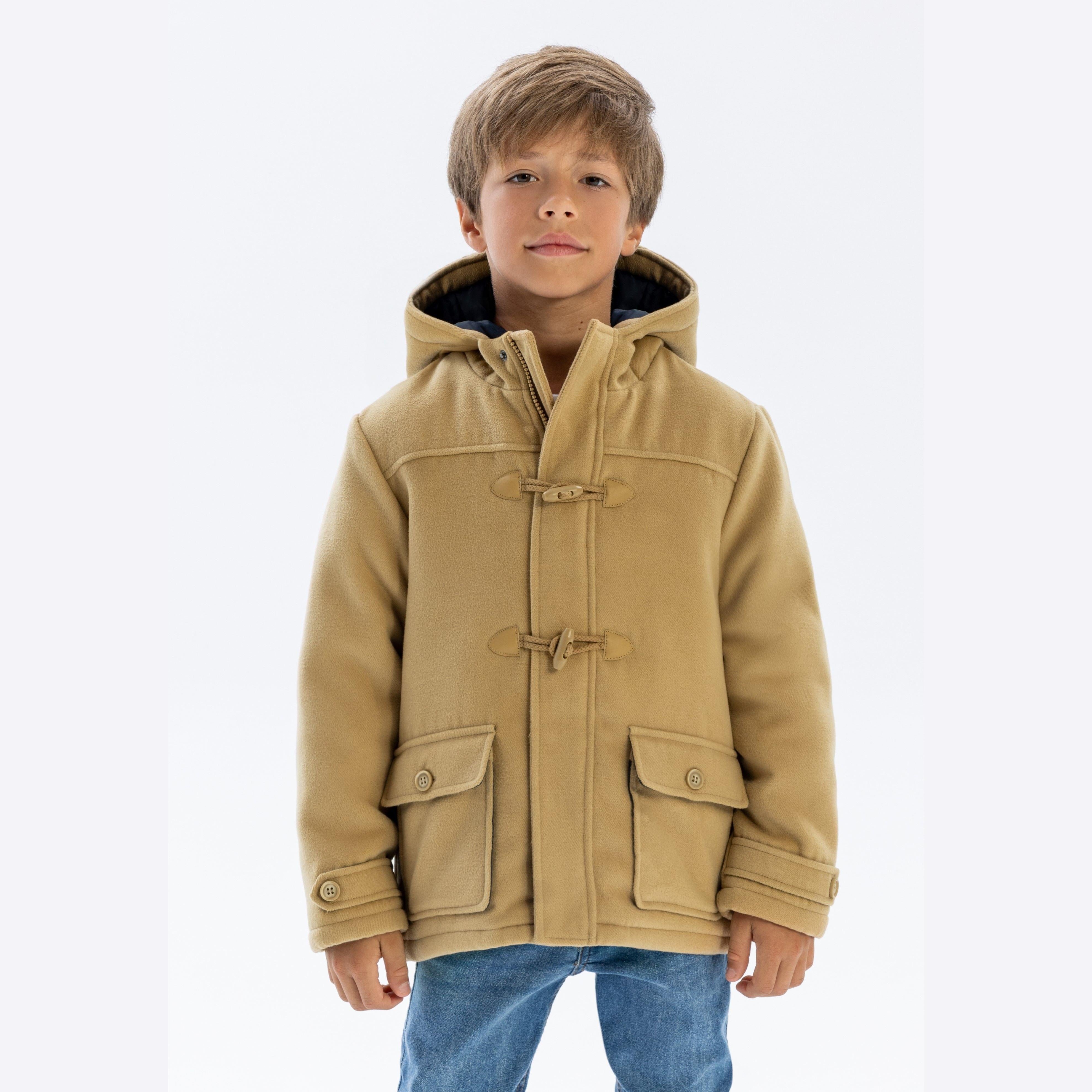 Young boy wearing beige duffle jacket with toggle fastenings and hood, paired with blue jeans, front view on white background