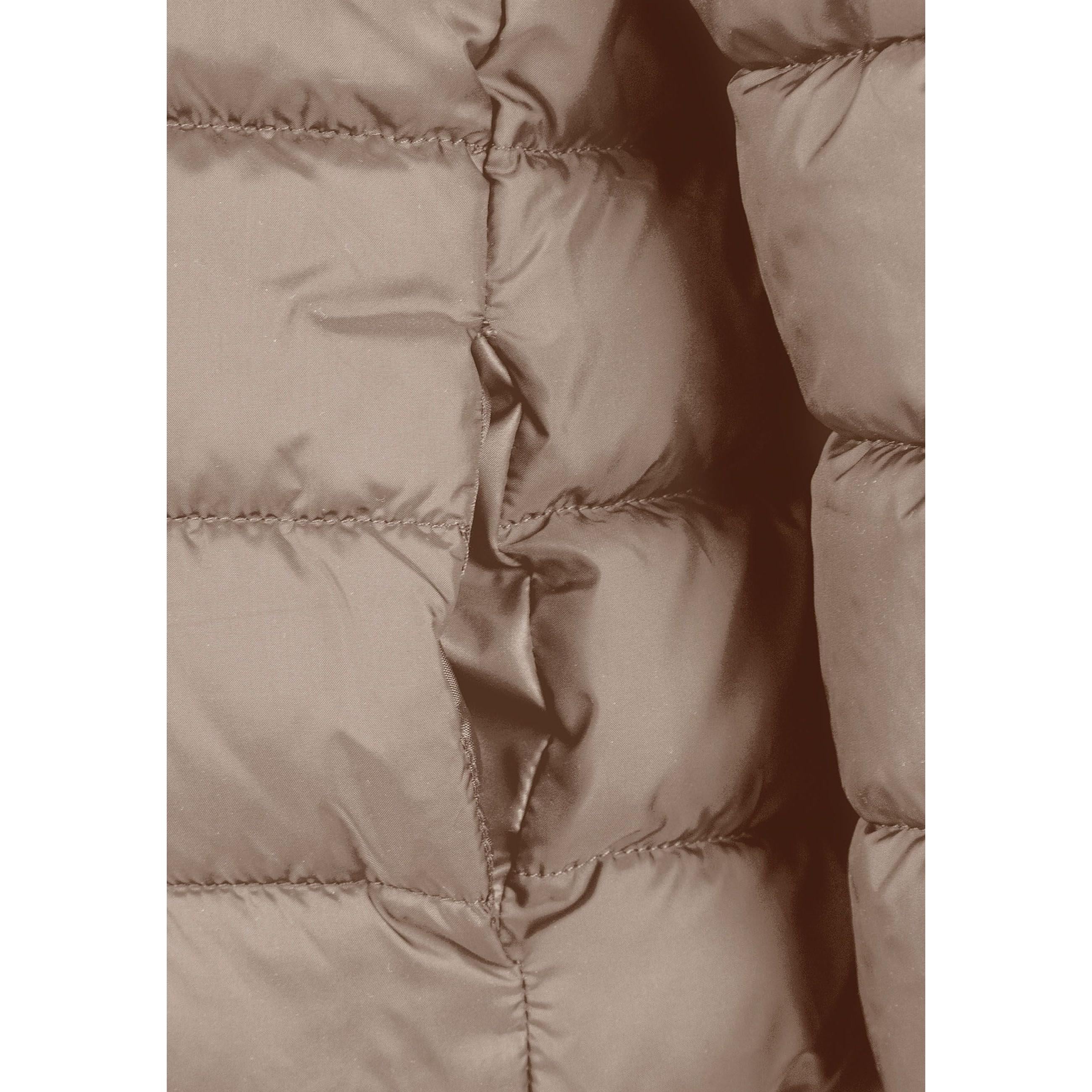 Detailed view of beige quilted jacket construction showing padded panels, zip mechanism and hood design elements, soft neutral lighting