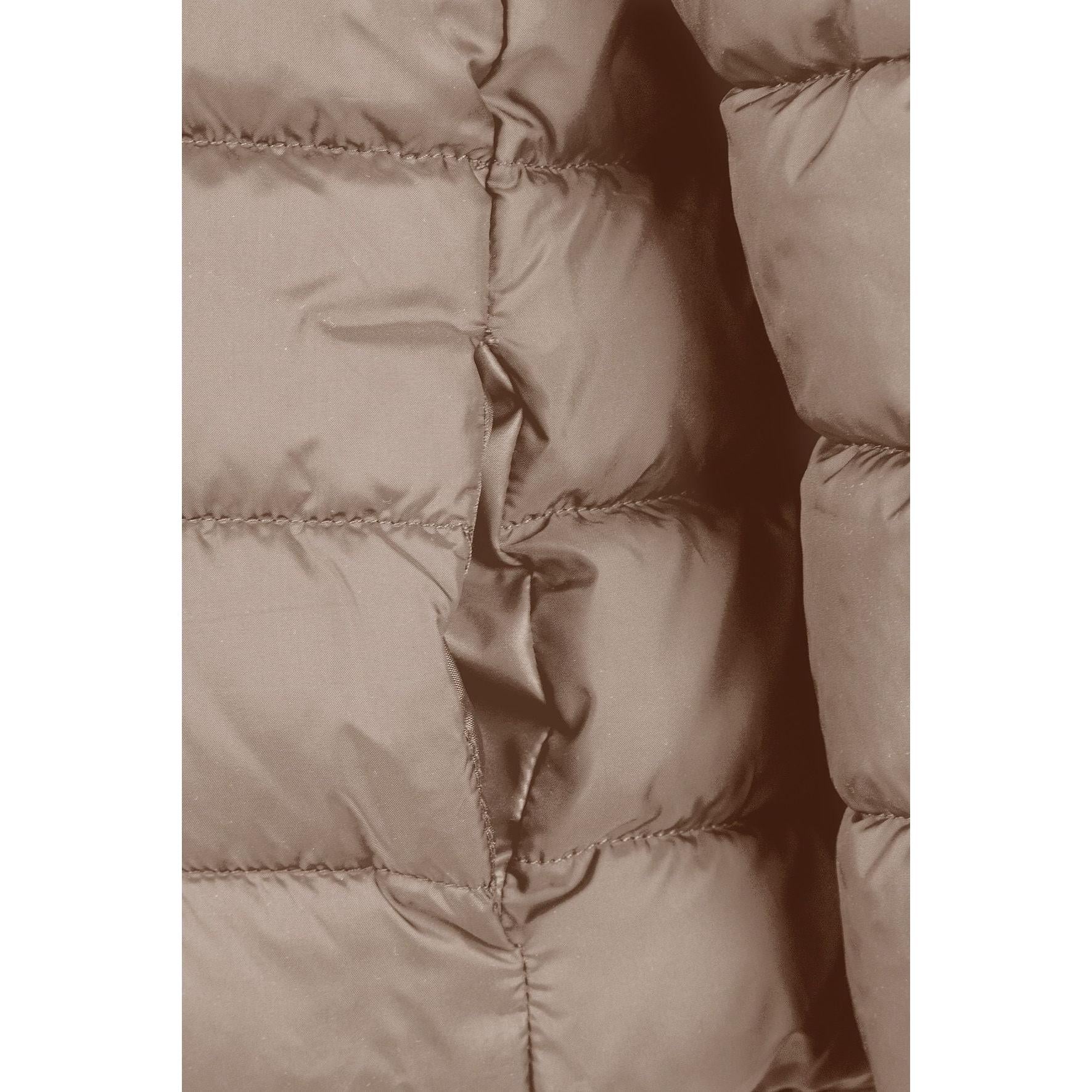 Detailed view of beige quilted jacket construction showing padded panels, zip mechanism and hood design elements, soft neutral lighting