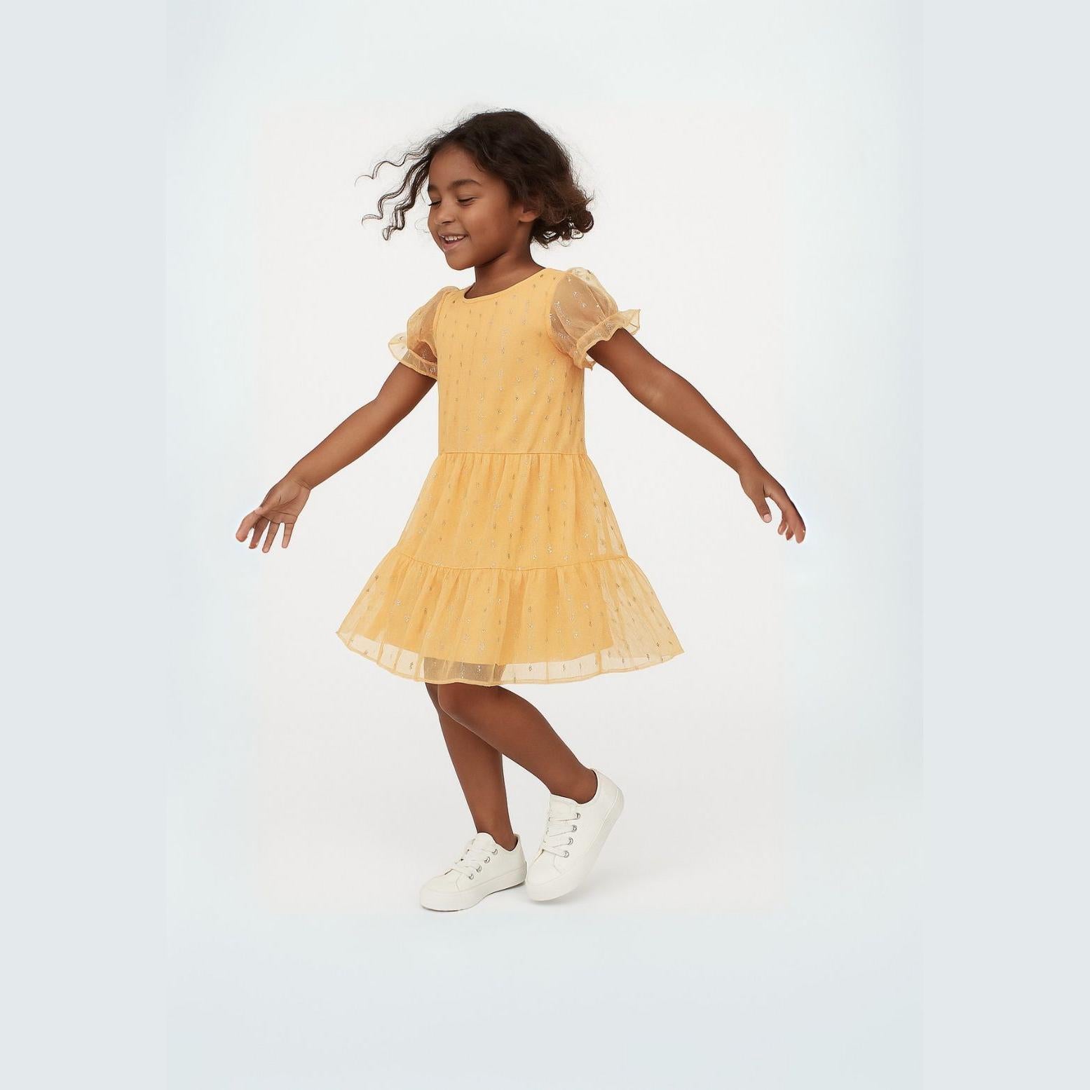 Young girl in motion wearing bright orange sparkle party dress with tiered tulle skirt, mesh sleeves, dancing pose against white studio background