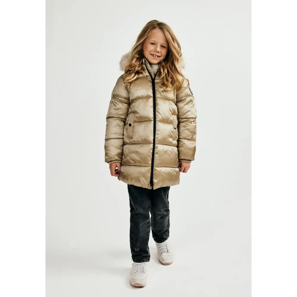 Same girl in gold quilted jacket walking pose, showing full length jacket design with hood up, dark wash jeans and white sneakers on white studio background