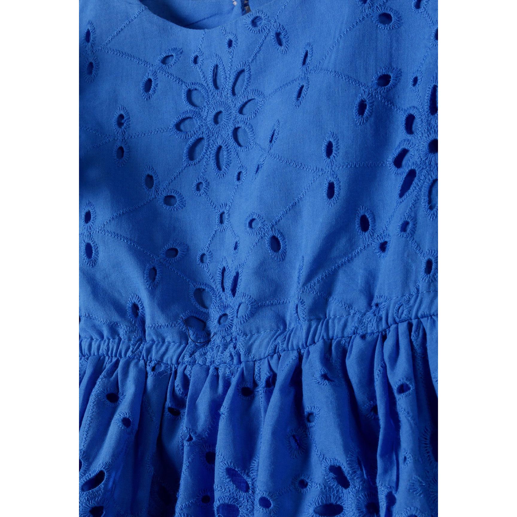 Close-up detail of blue broderie anglaise fabric showing floral embroidered cut-out pattern and gathered waist seam