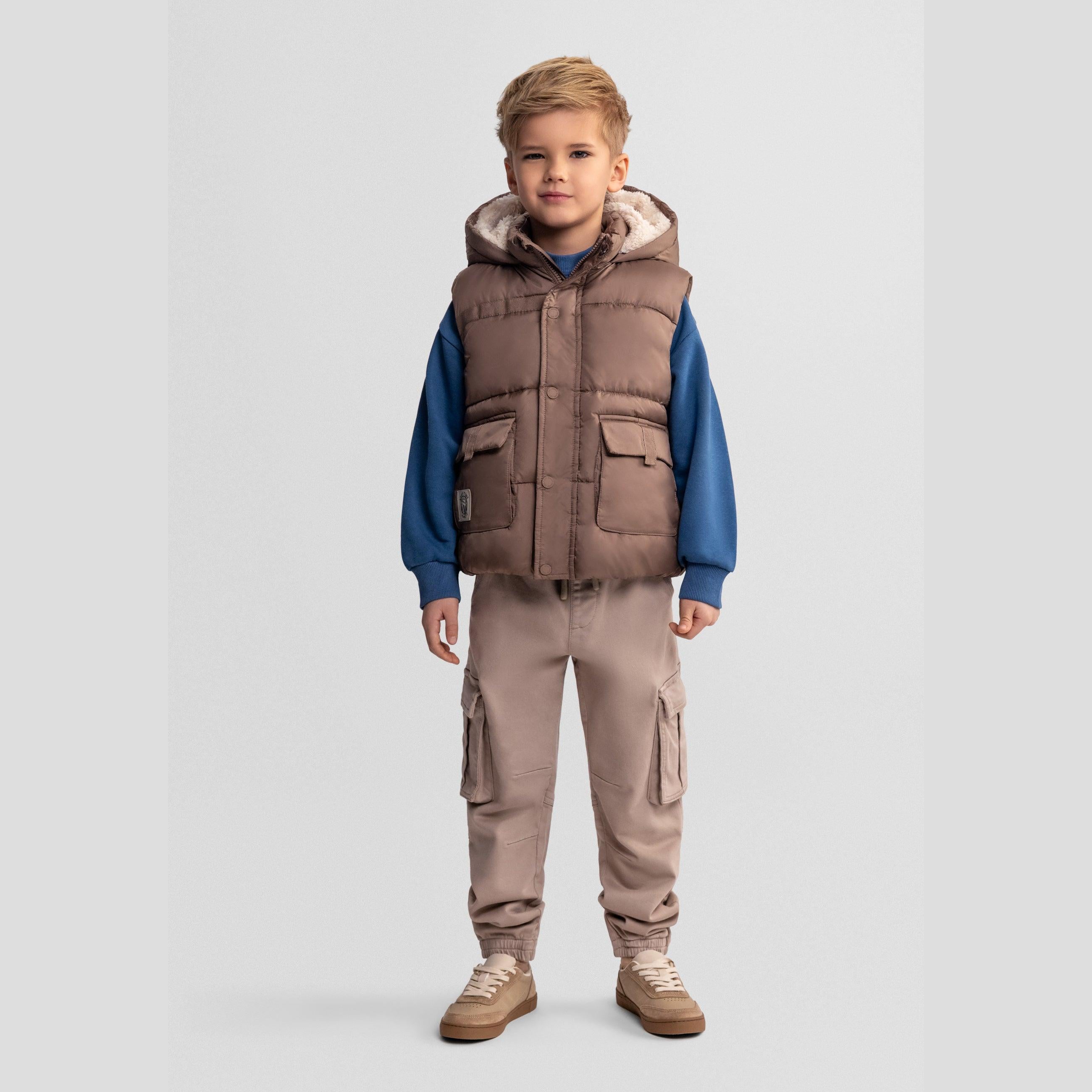 Front view of boy wearing beige quilted hooded gilet over blue sweatshirt with beige cargo trousers on grey background