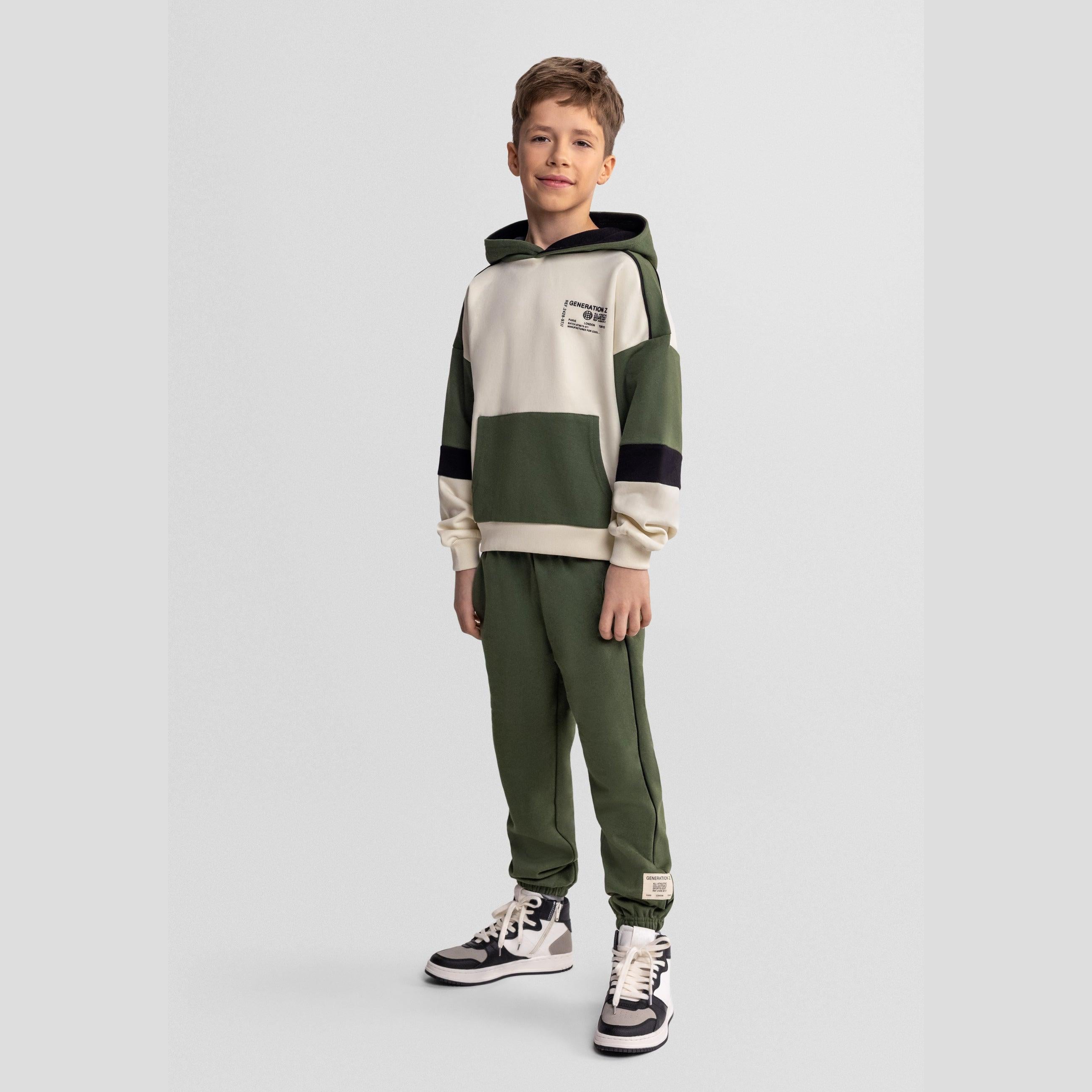 Boy wearing khaki tracksuit set with hooded sweatshirt and joggers against light background, full body front view