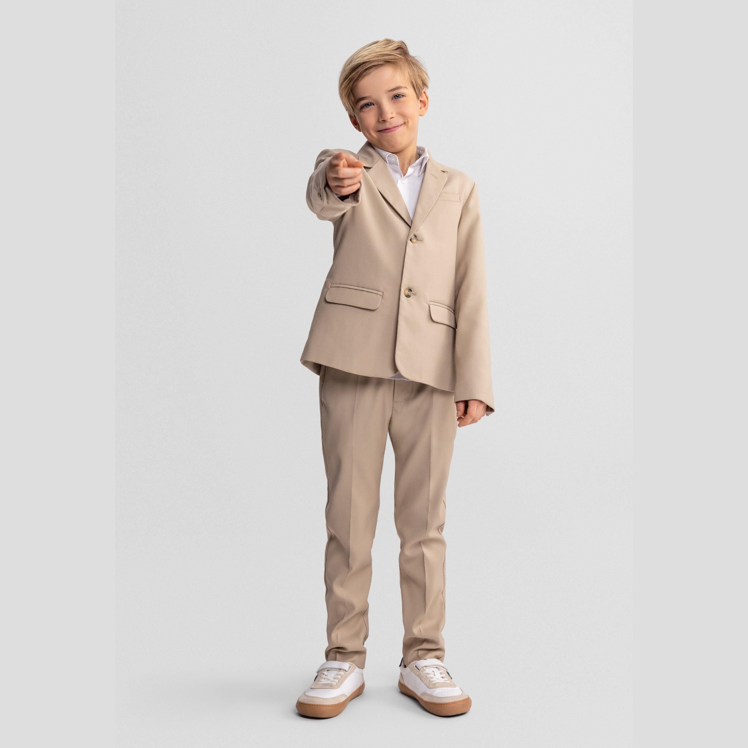 Full length view of boy in complete stone suit pointing at camera, wearing white trainers against grey studio background
