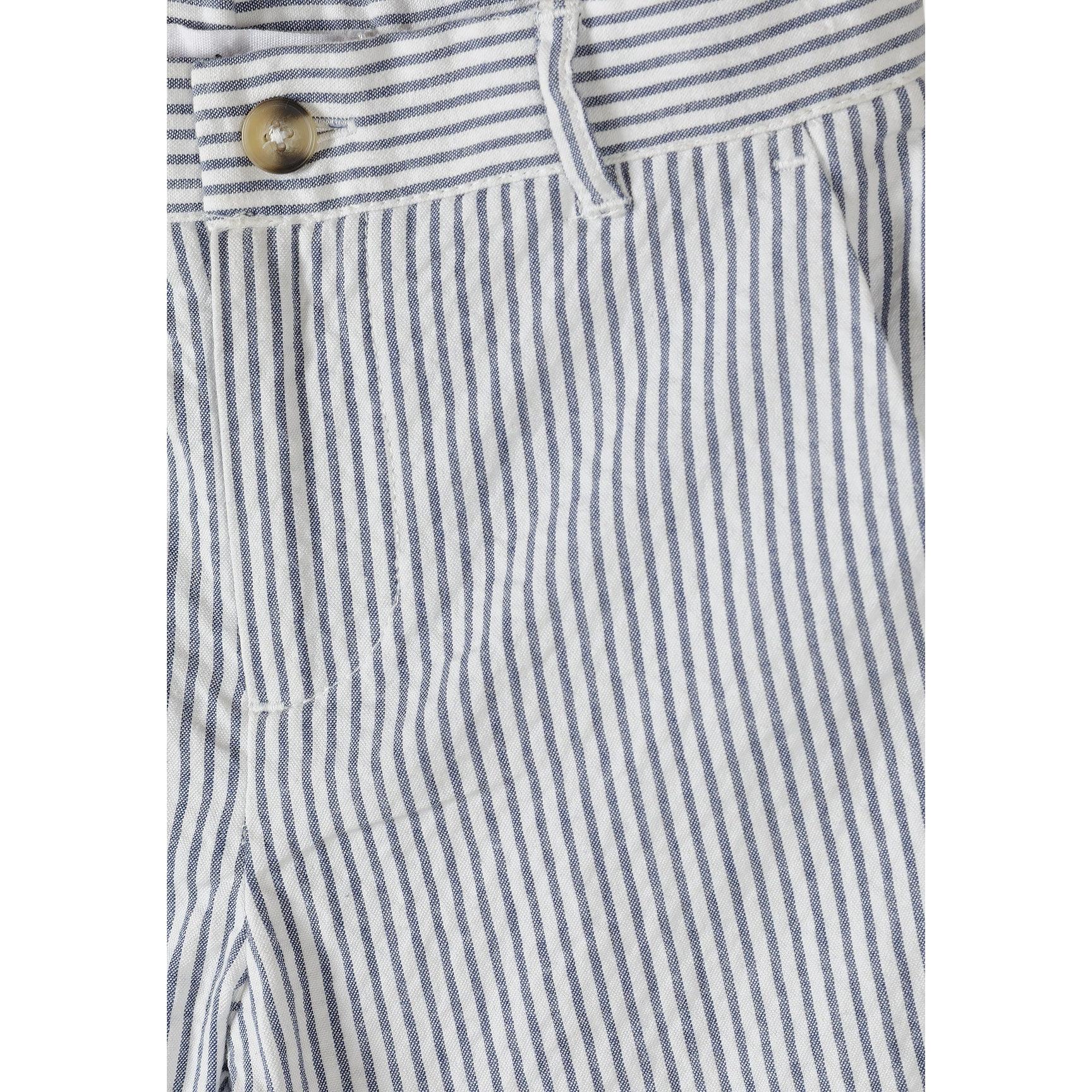 Boy in navy striped blazer and matching shorts with white top, posing with one hand on hip against light grey studio background