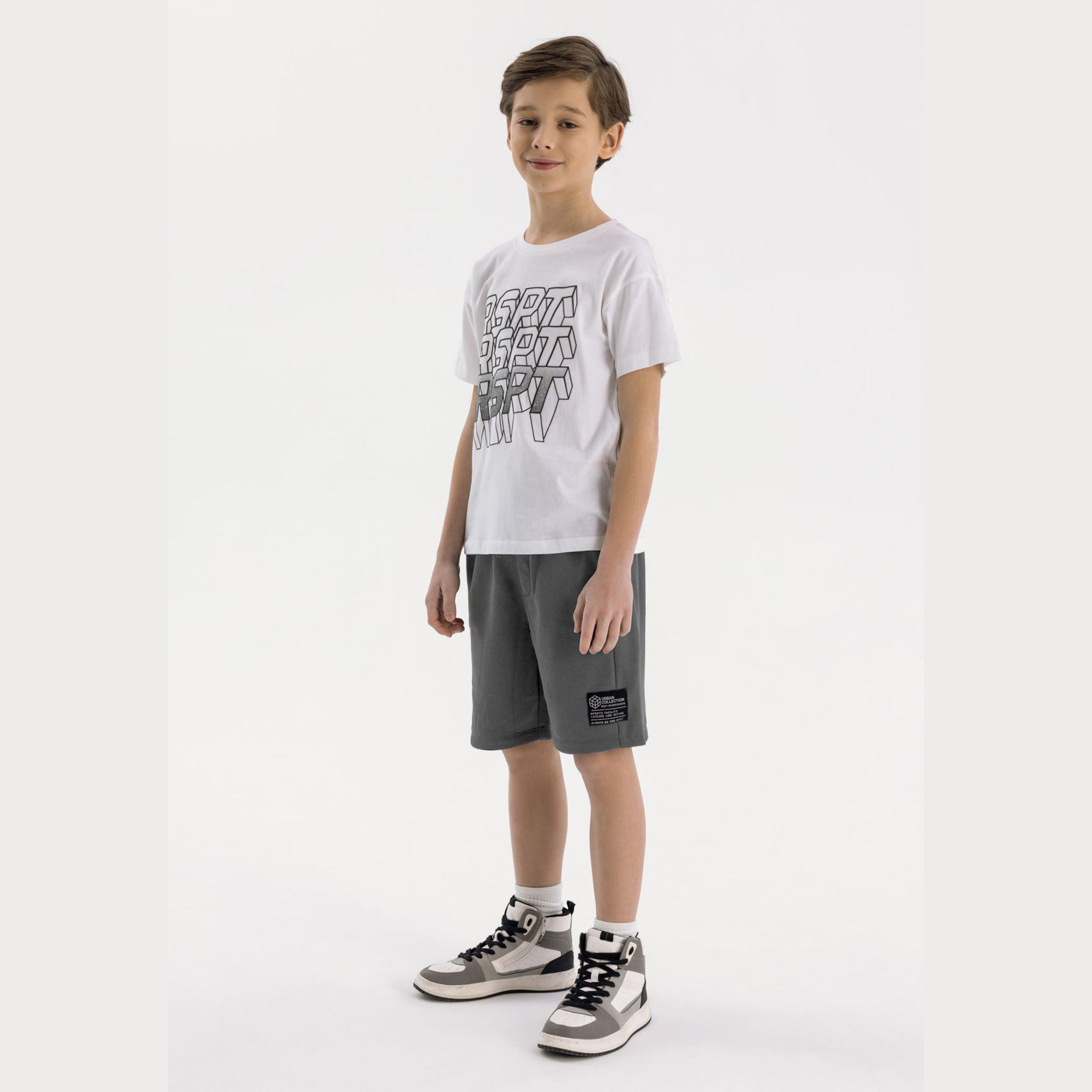 Young boy wearing white graphic t-shirt and grey fleece shorts with ribbed side panels, paired with grey and white sneakers, standing against white background