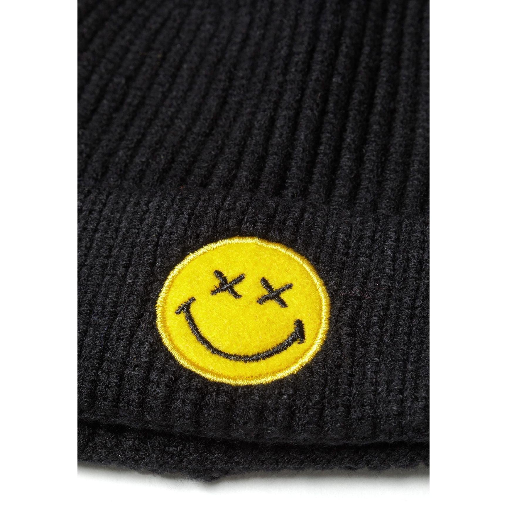 Close-up detail of yellow embroidered smiley face badge with cross eyes on black ribbed knit fabric
