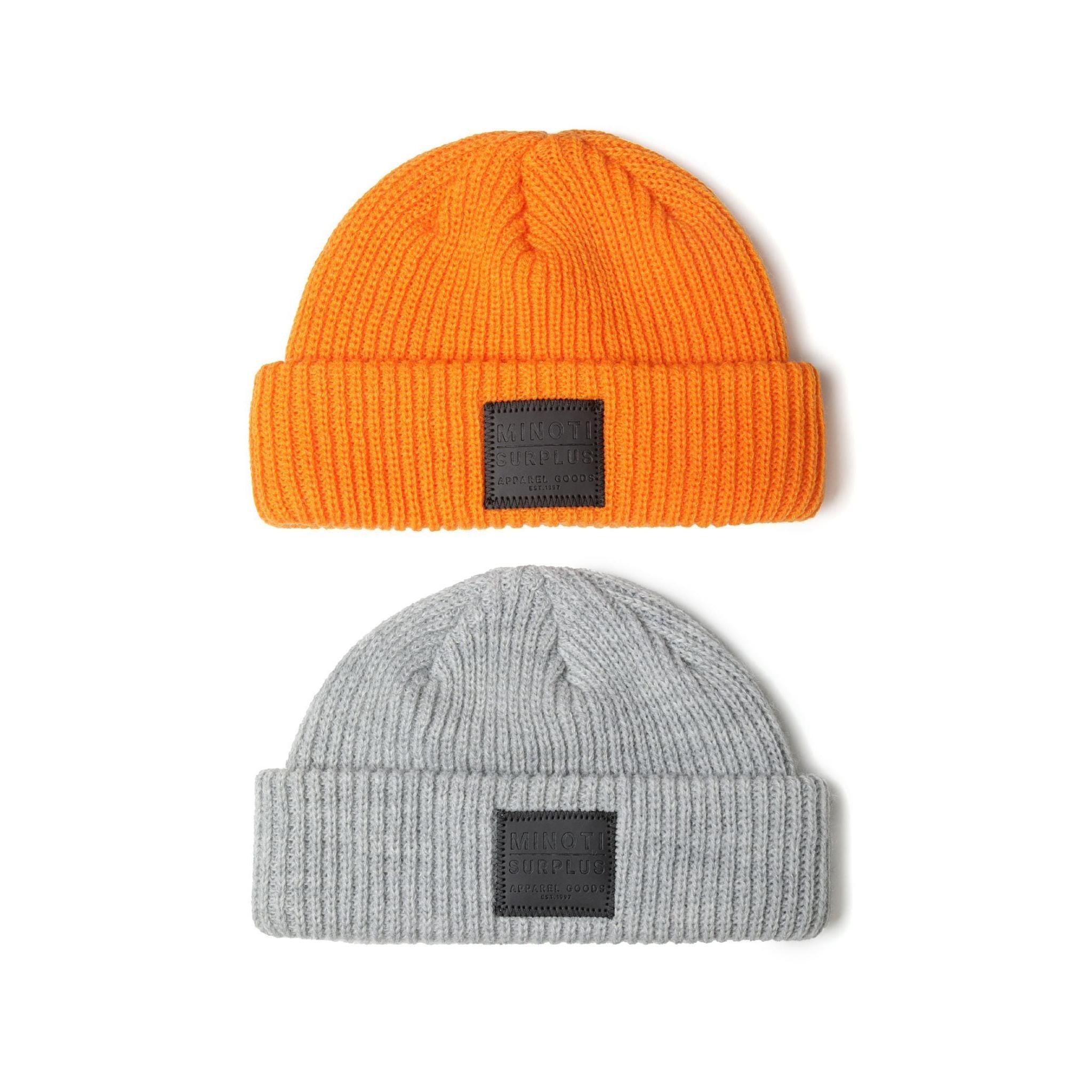 Two ribbed knit beanies on white background - bright orange beanie with dark grey rectangular patch on top, light grey beanie with dark patch below