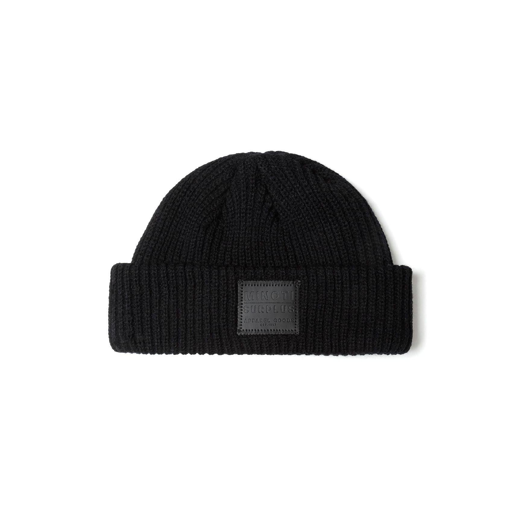 Detail view of burgundy beanie folded to show the ribbed knit texture and Minoti Surplus rectangular patch label with embossed lettering on the front