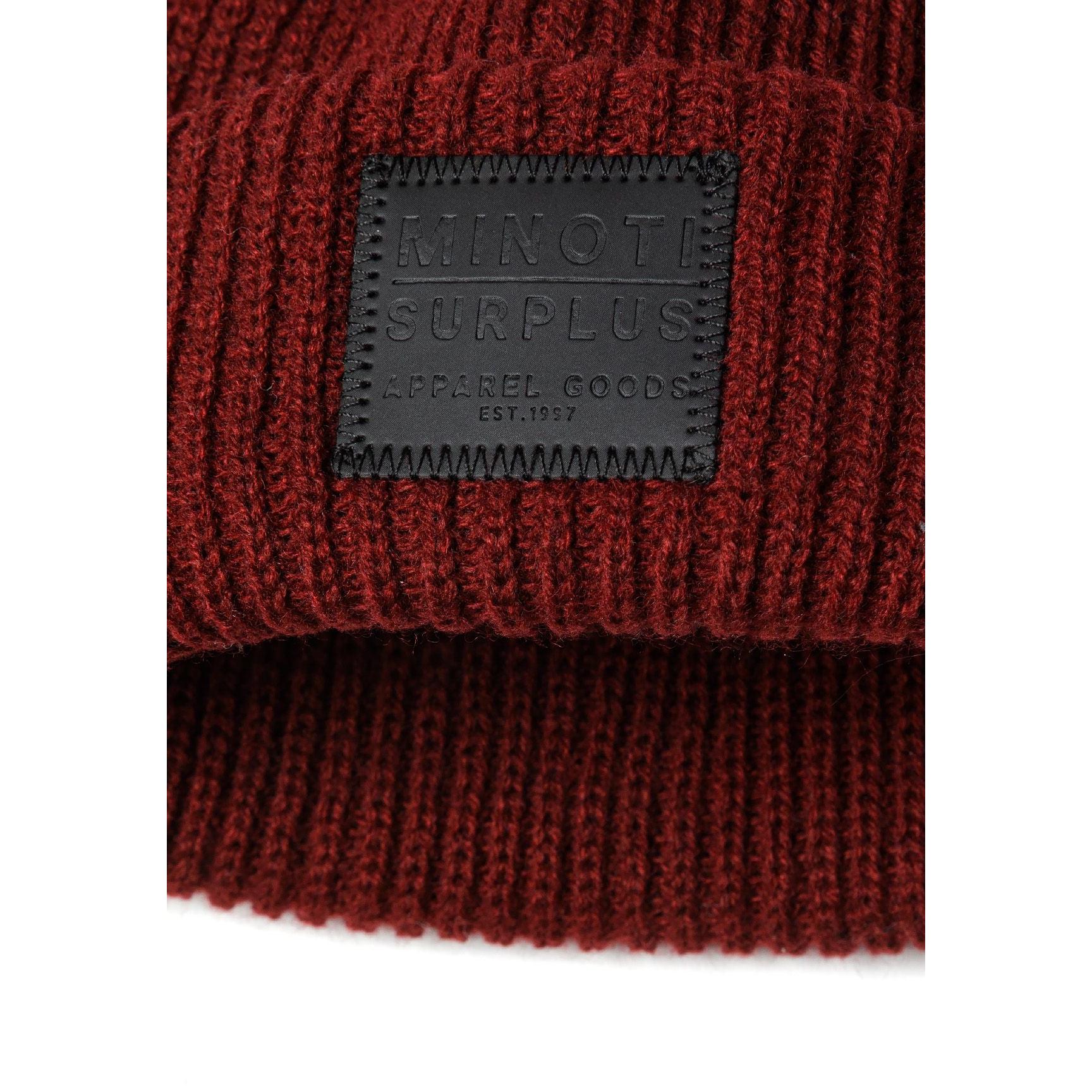 Detail view of burgundy beanie folded to show the ribbed knit texture and Minoti Surplus rectangular patch label with embossed lettering on the front