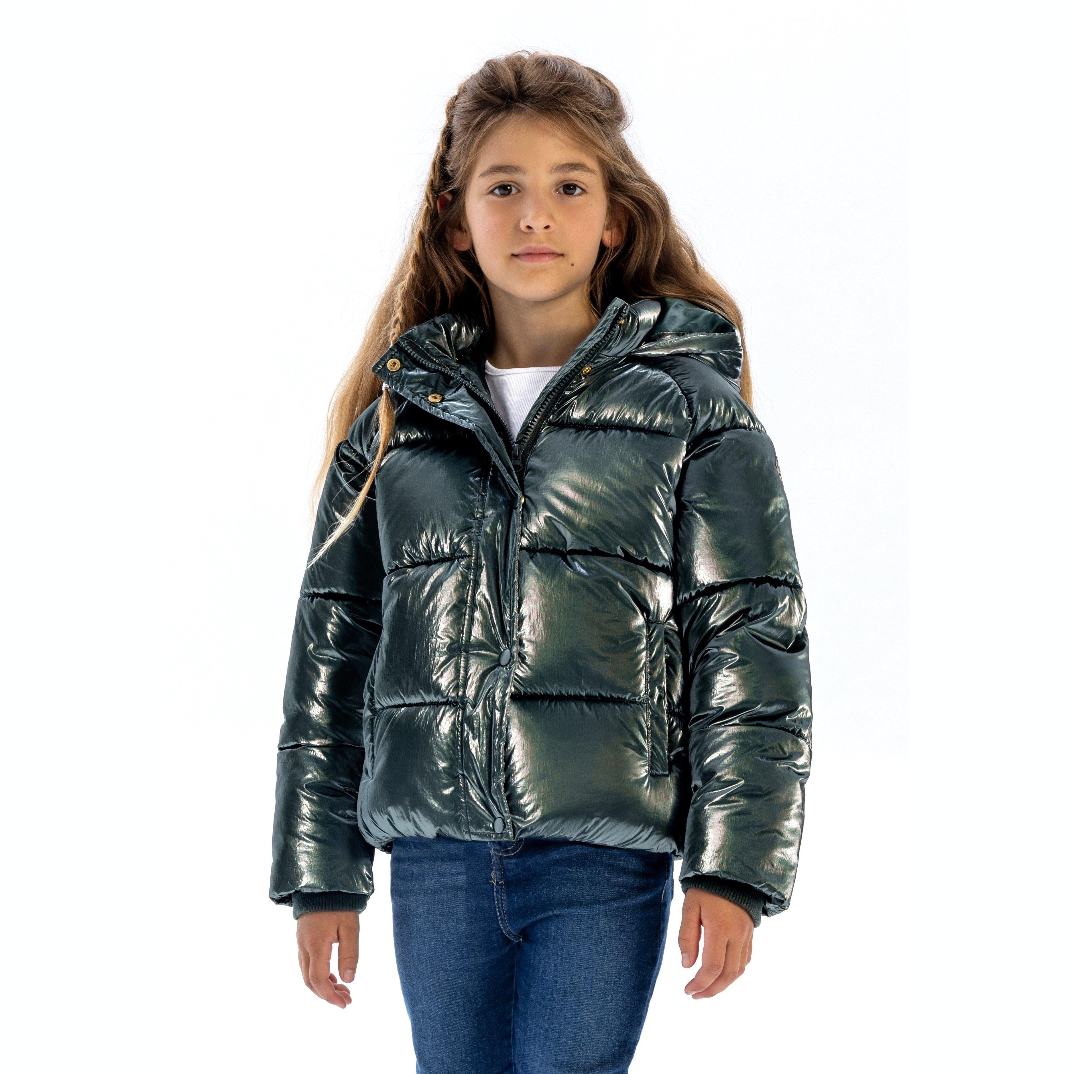 Young girl wearing shimmering green quilted padded jacket with hood and blue jeans against white background