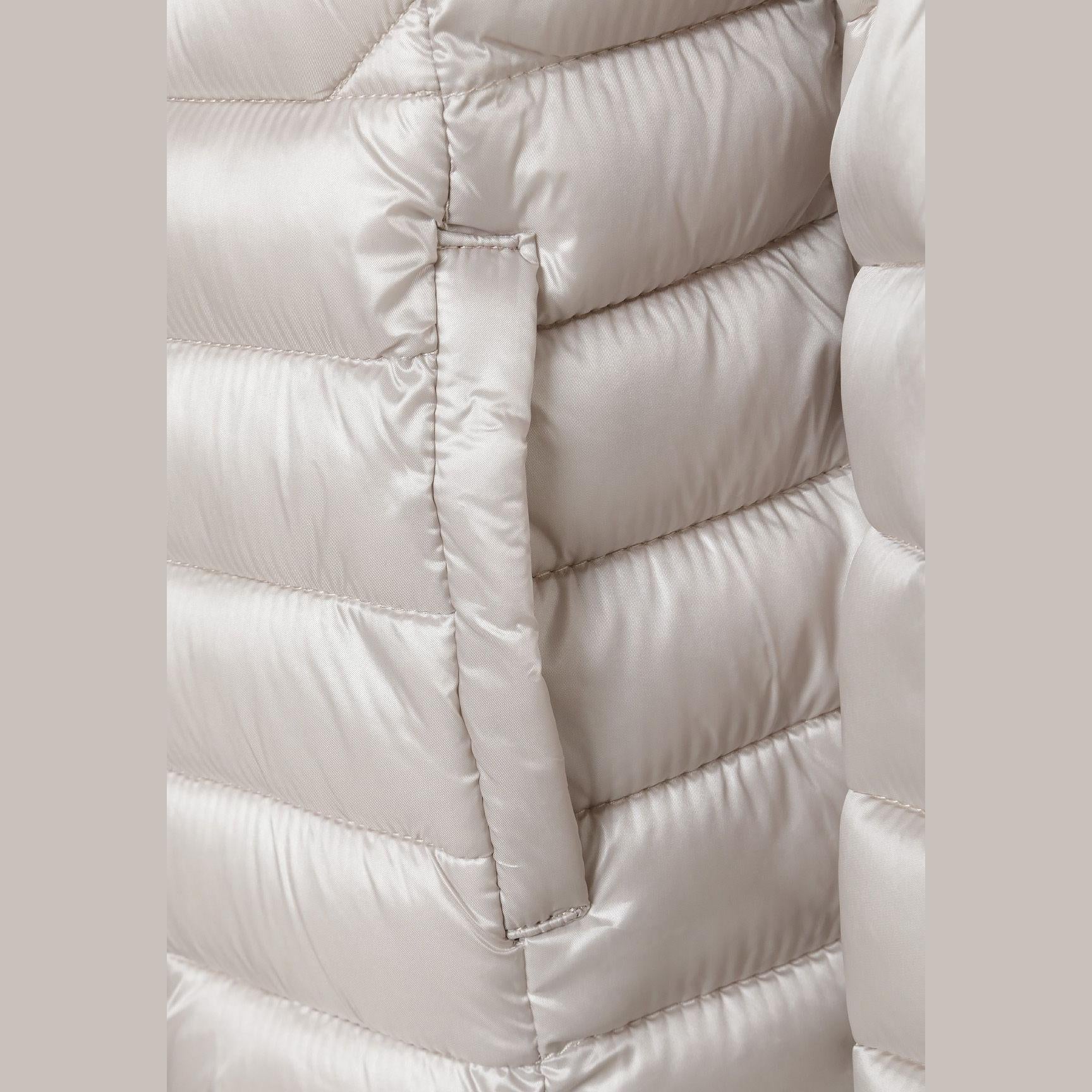 Close-up detail of grey quilted jacket showing circular embroidered patch with heart design and quilted texture