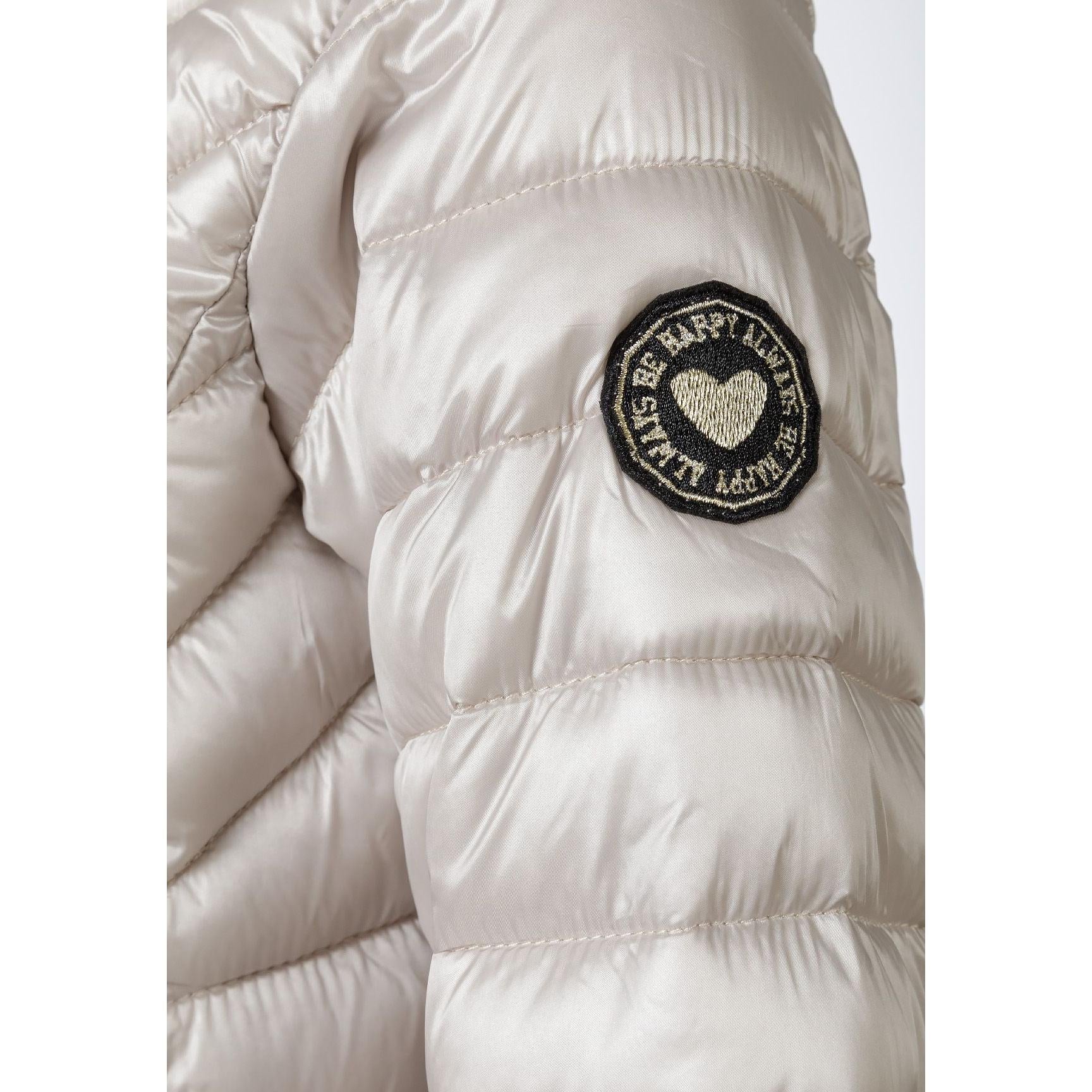 Close-up detail of grey quilted jacket showing circular embroidered patch with heart design and quilted texture