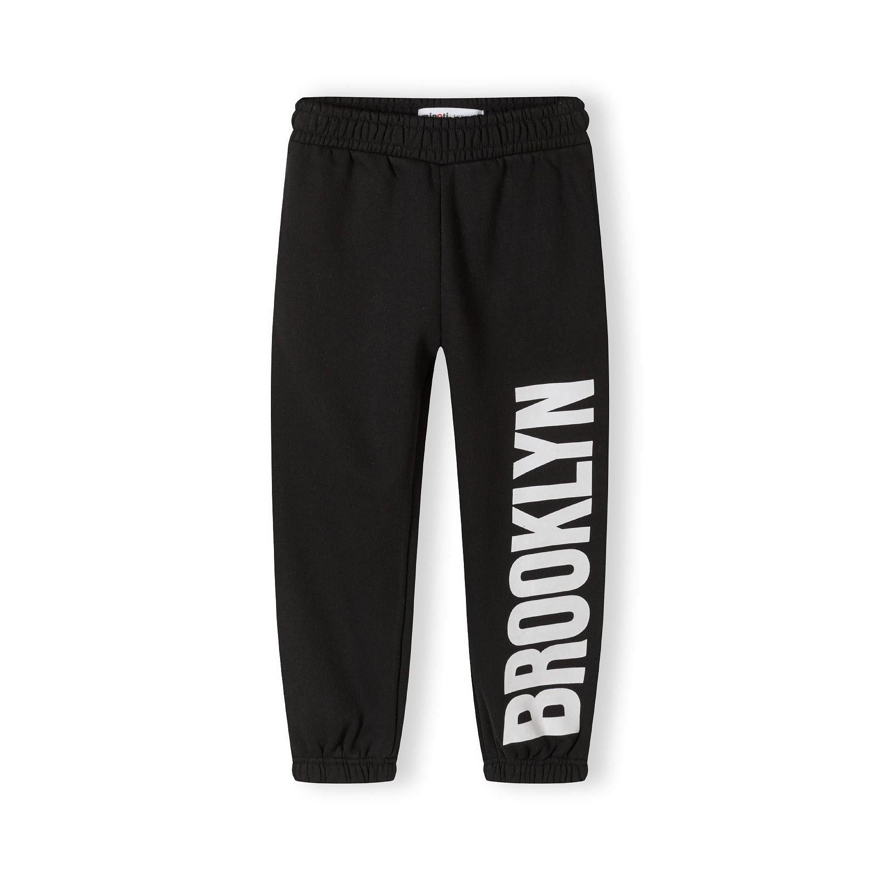 Close-up detail of black tracksuit joggers showing ribbed waistband and white text print on leg