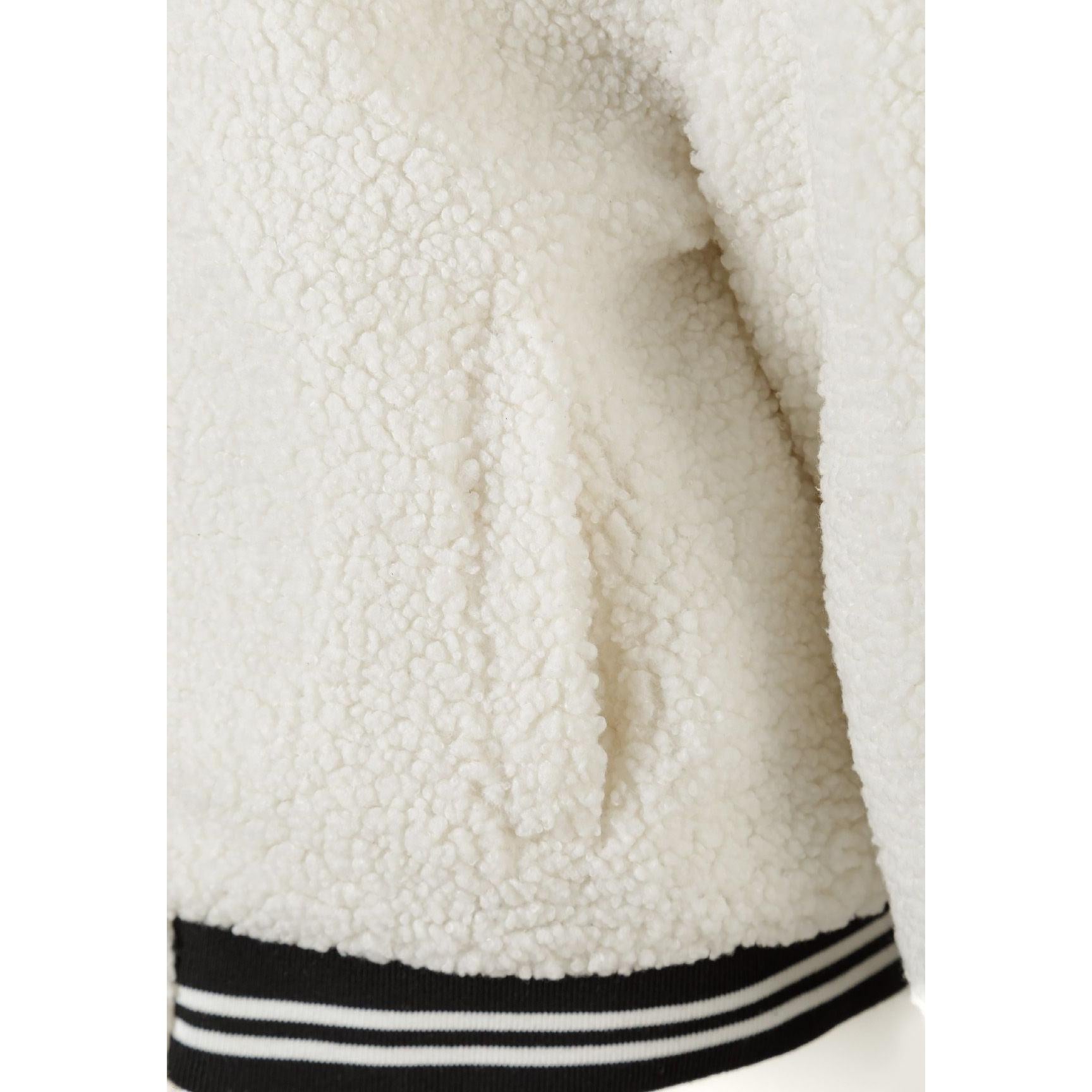 Close-up detail of embroidered letter M on cream borg fabric showing black outline stitching against textured surface