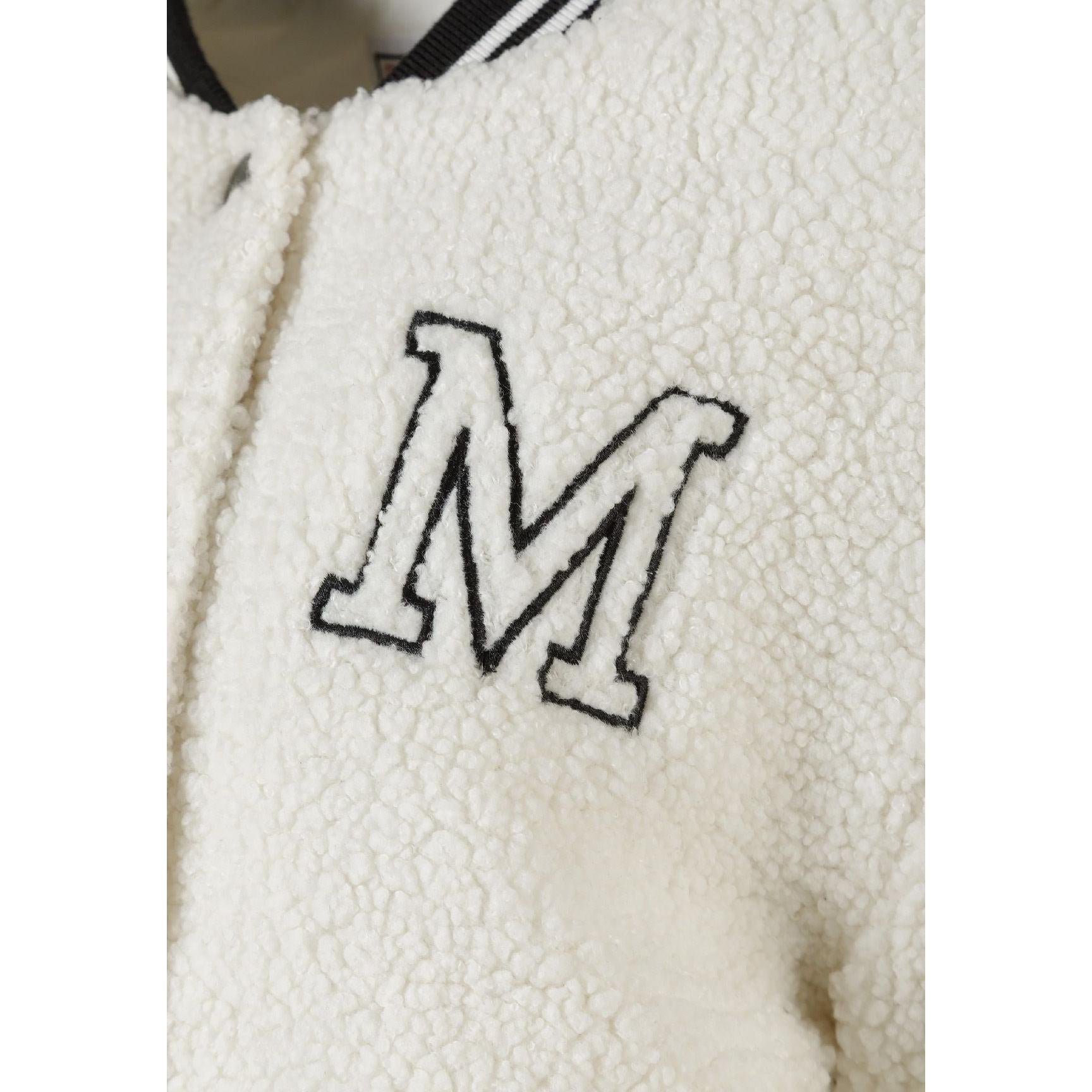 Close-up detail of embroidered letter M on cream borg fabric showing black outline stitching against textured surface