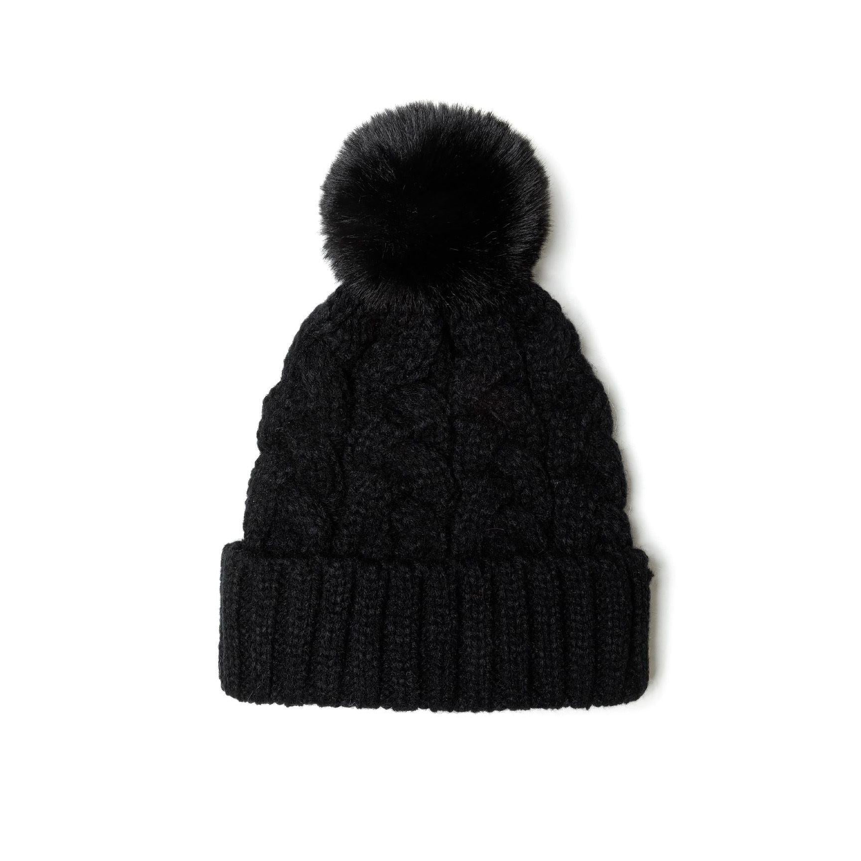 Close-up detail of black cable knit hat showing textured knit pattern and fluffy black pom pom against white background