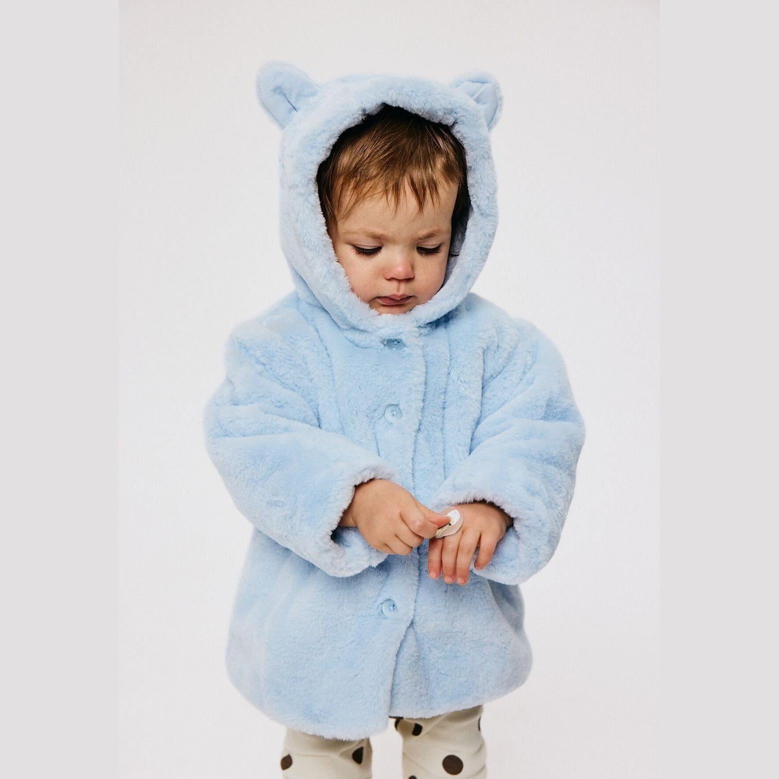 Baby wearing light blue plush faux fur jacket with 3D ears hood, button front fastening, shown against neutral background