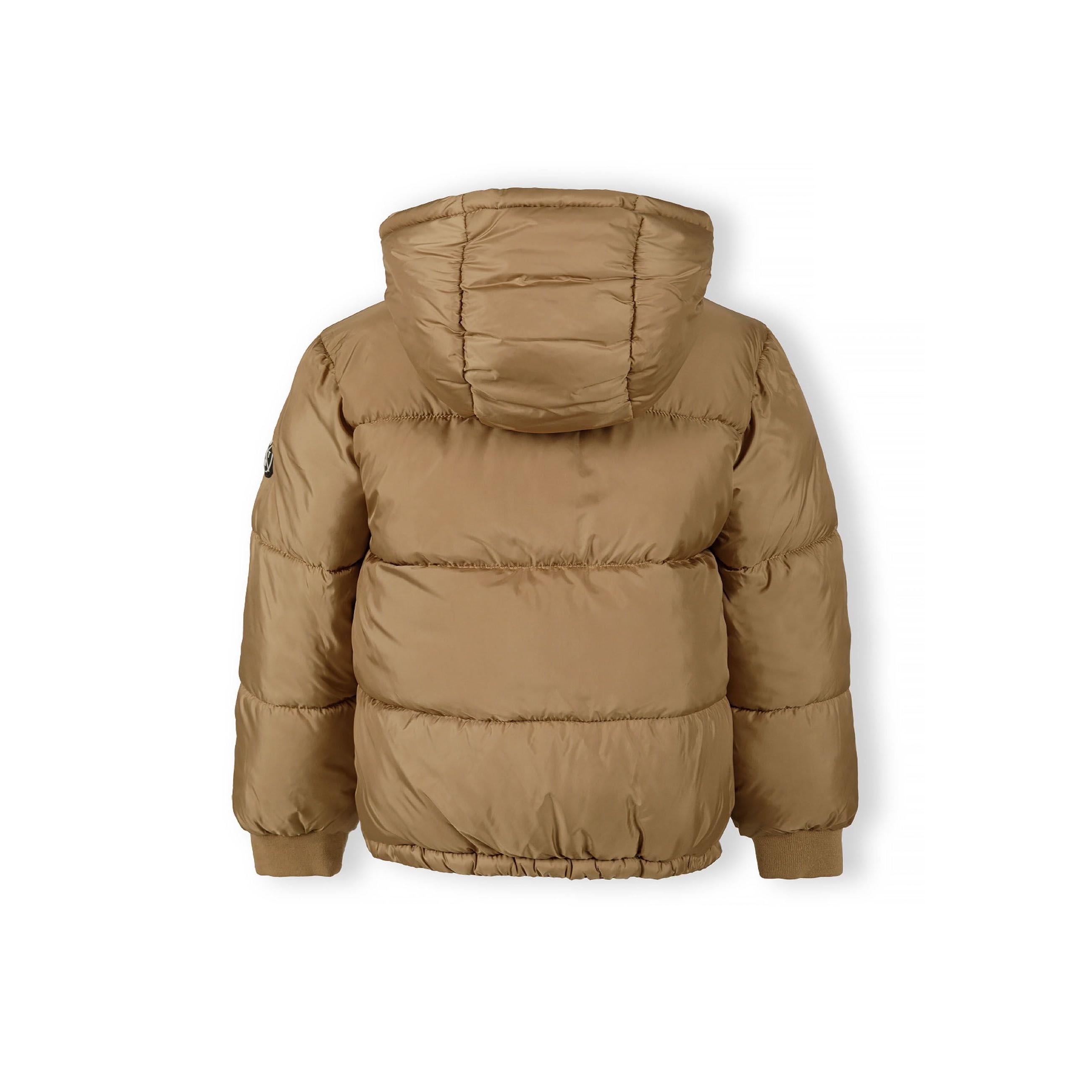 Close-up of black circular badge with white cross design showing letters M, N, T and number 97 on beige jacket fabric