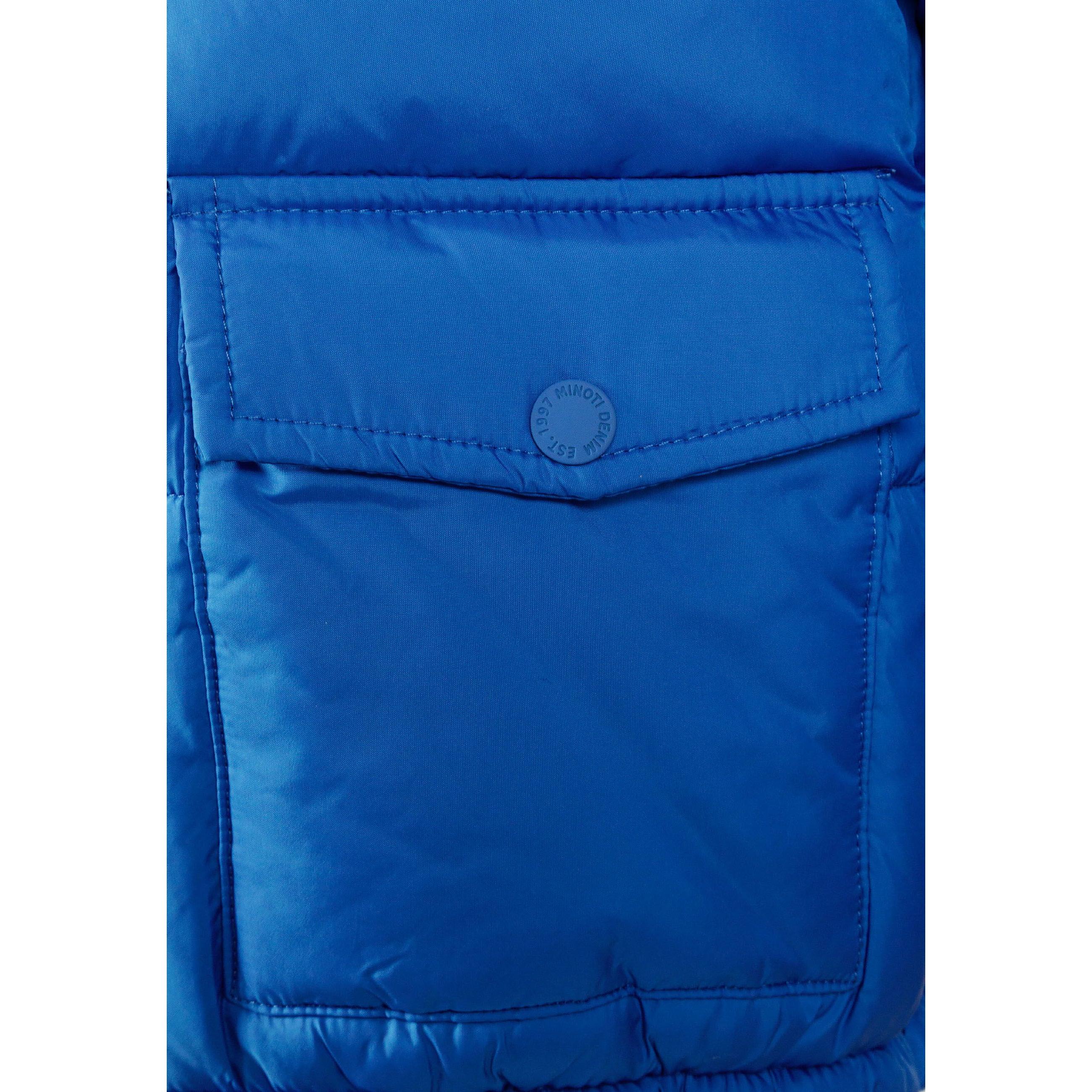 Close-up detail of cobalt blue jacket sleeve showing circular black patch with white crossed lines and letters M, N, T, 97