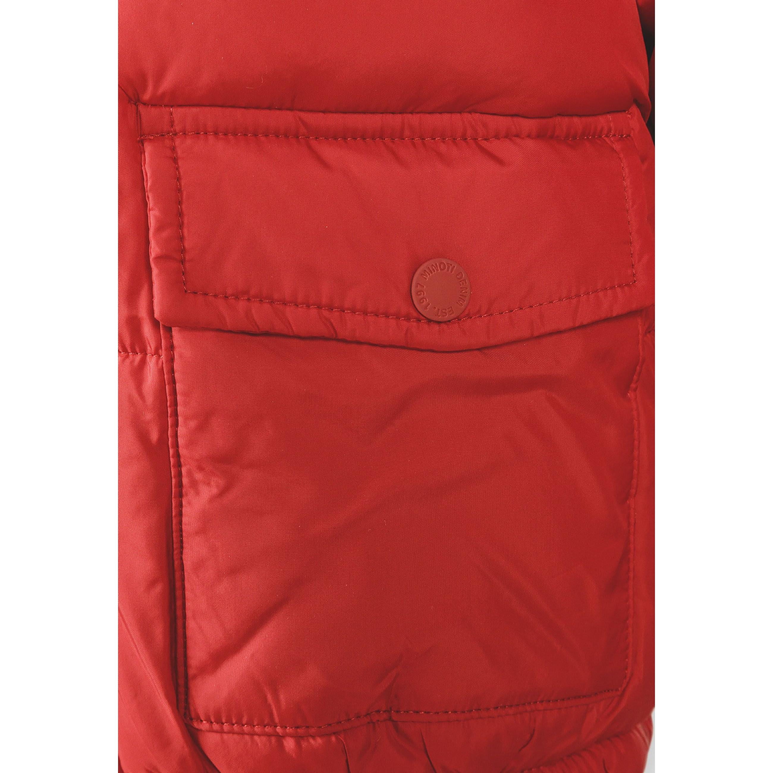 Close-up detail of black circular logo patch with white crossed lines and letters M N T 97 on red jacket sleeve