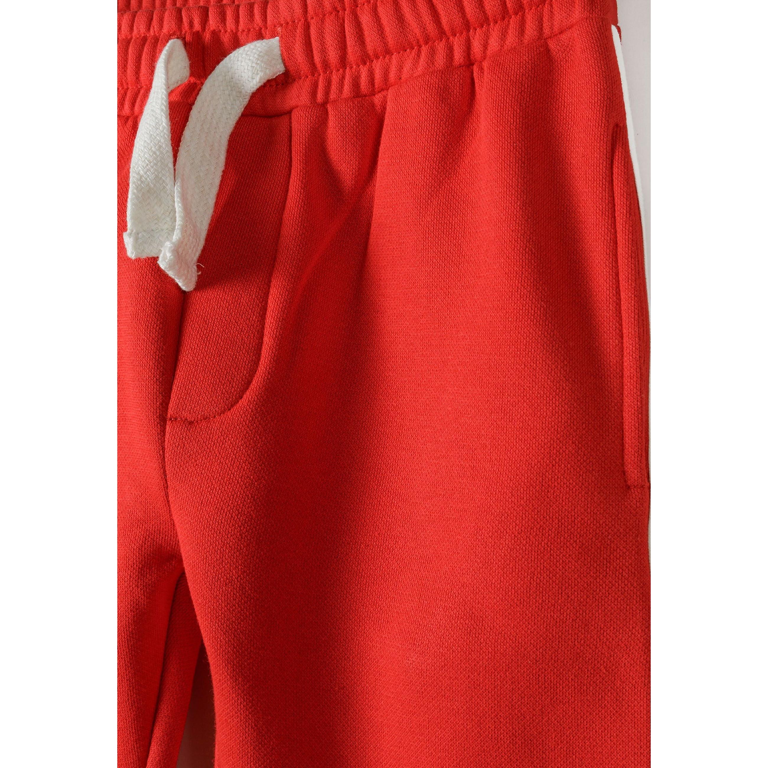 Close-up detail of red joggers showing white drawstring ties and front pocket construction