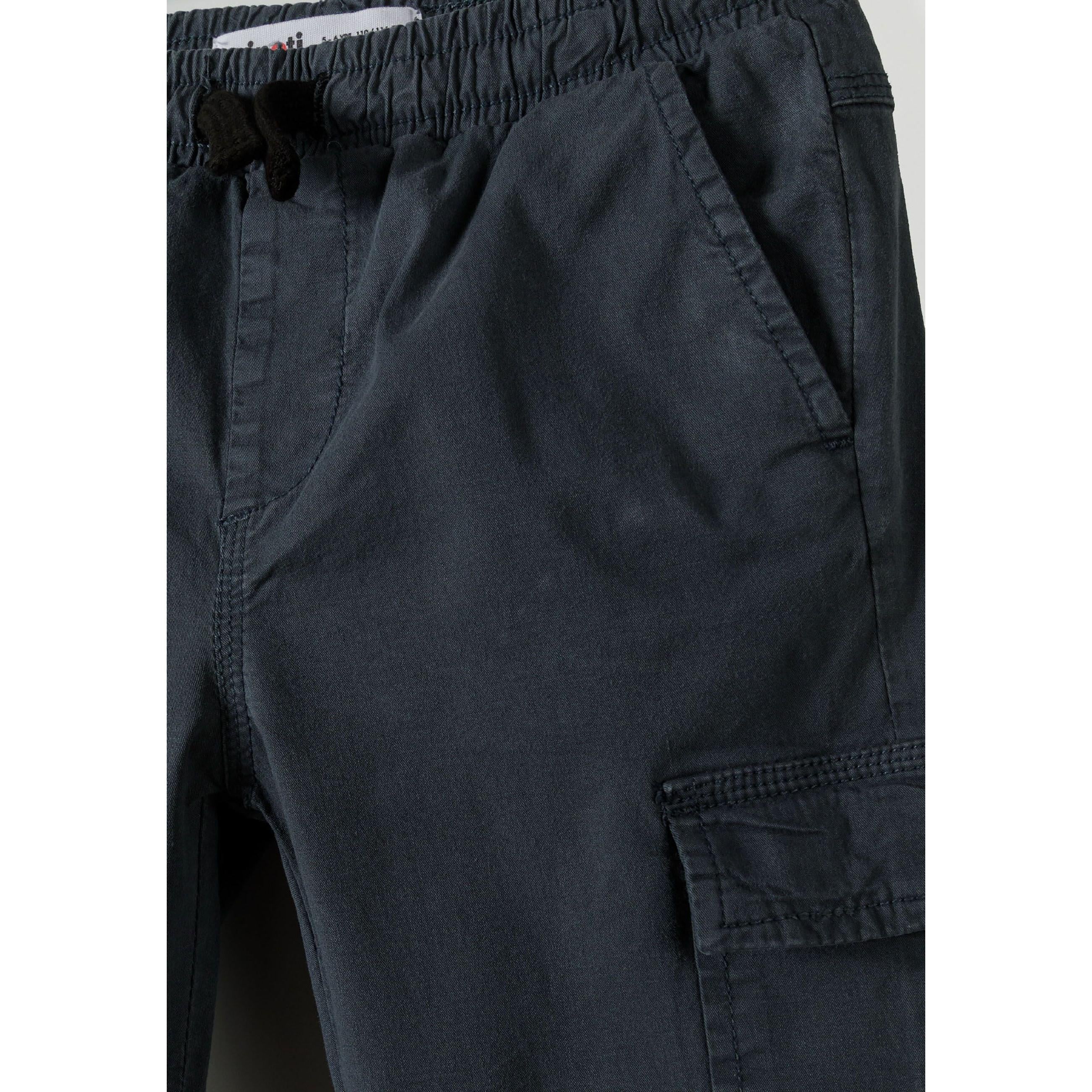 Close-up detail of navy cargo trousers showing elasticated waistband, side cargo pocket with flap closure on white background