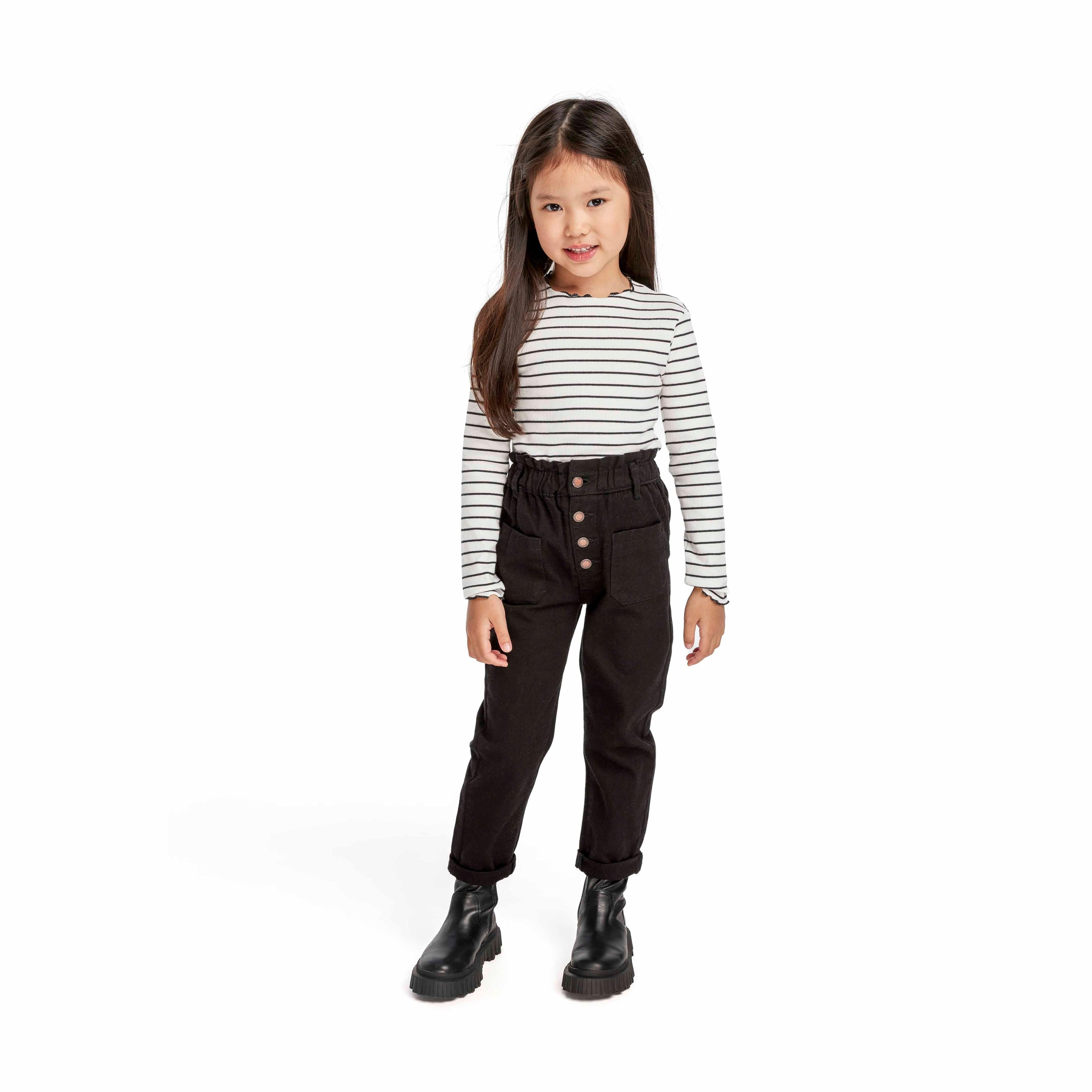 Young girl wearing black paperbag waist jeans with striped long-sleeve top and black boots, full body pose on white background